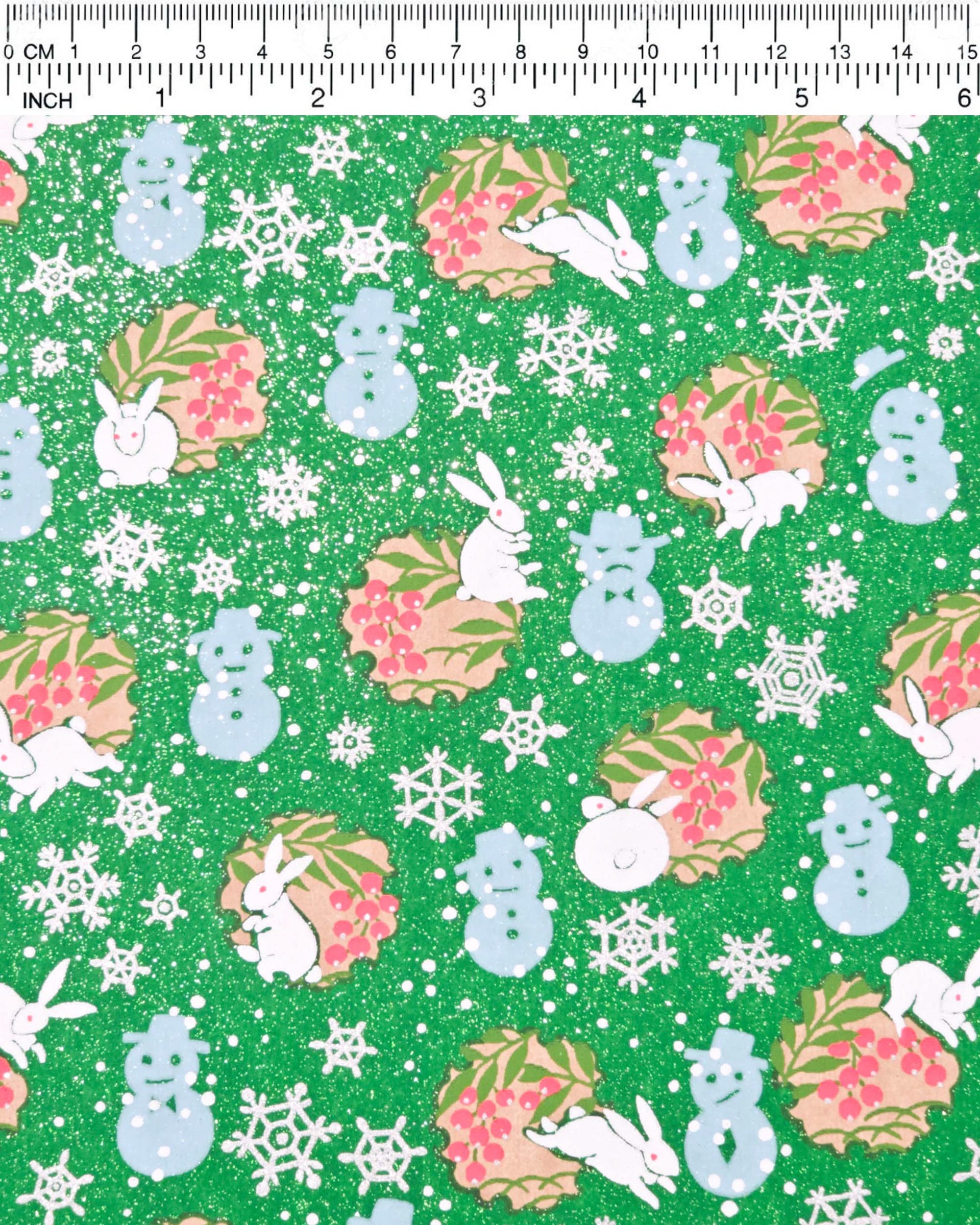 Japanese chiyogami paper featuring light blue snowmen, white rabbits, silver snowflakes, and brown yukiwas with red berries inside on a glitter green background.