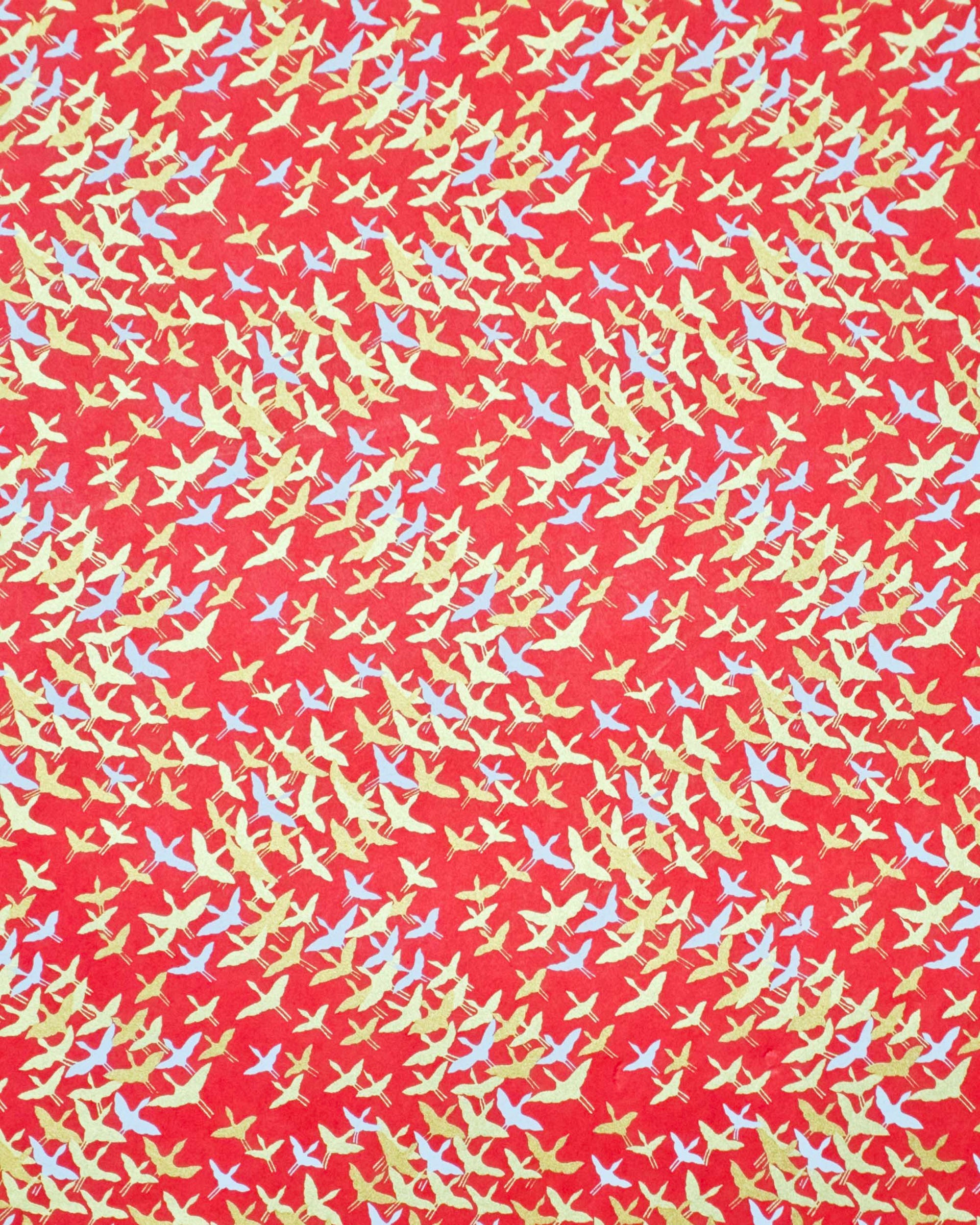 Japanese chiyogami paper featuring small white and metallic gold flying cranes in a zigzag formation on a red background.