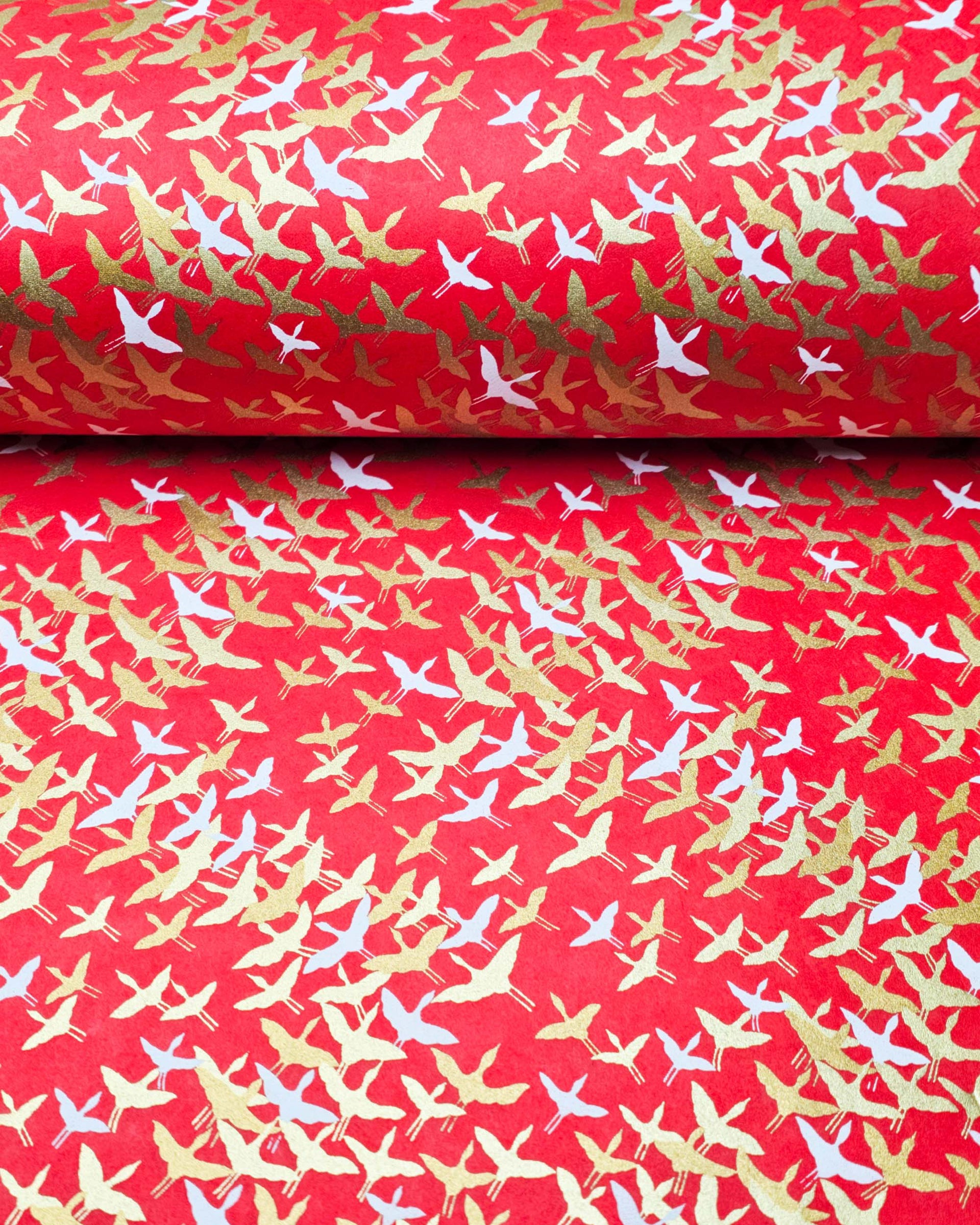Japanese chiyogami paper featuring small white and metallic gold flying cranes in a zigzag formation on a red background.