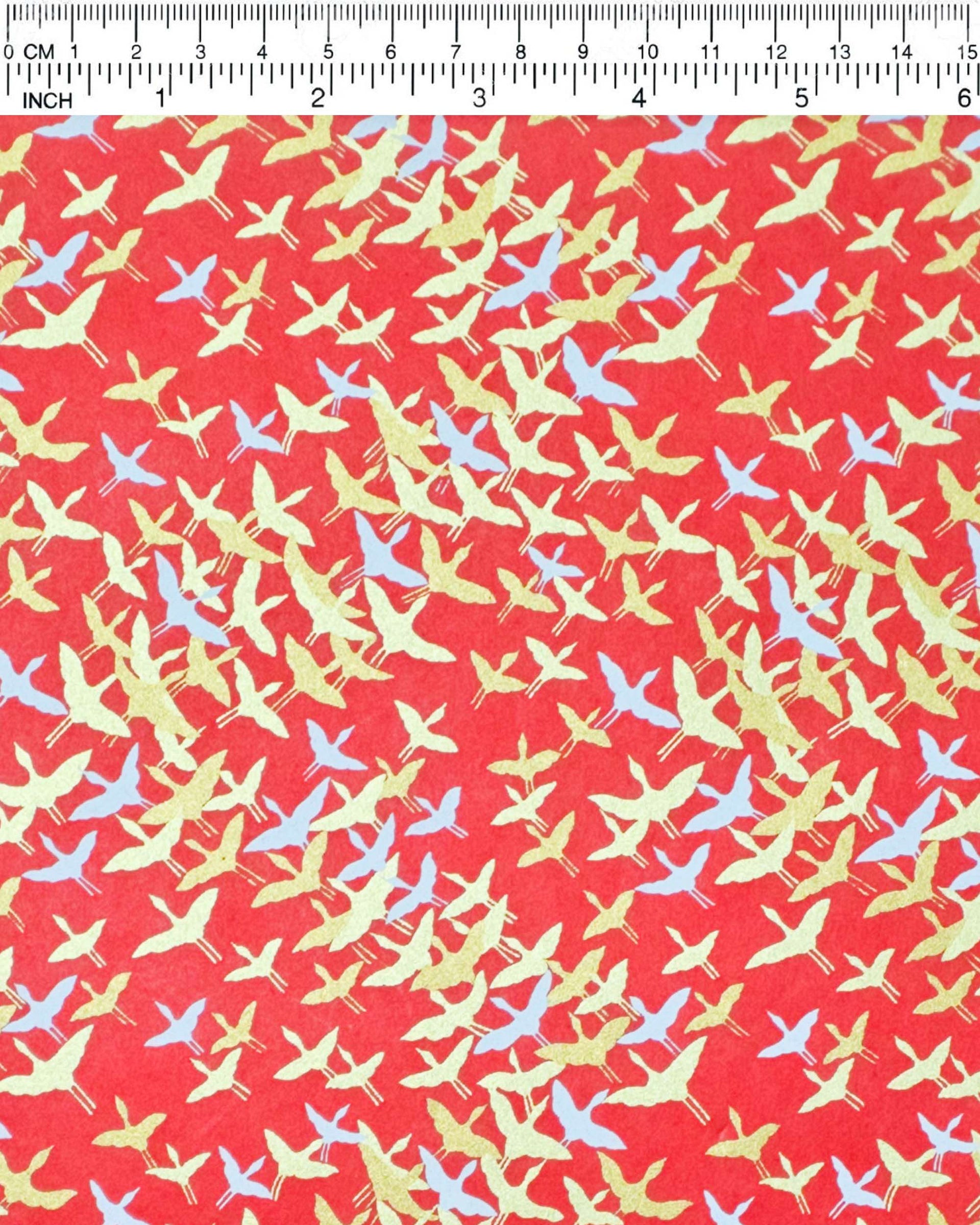 Japanese chiyogami paper featuring small white and metallic gold flying cranes in a zigzag formation on a red background.