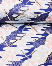 Japanese chiyogami paper featuring black and white katana swords with white and light pink cherry blossoms on a blue background with metallic gold details.