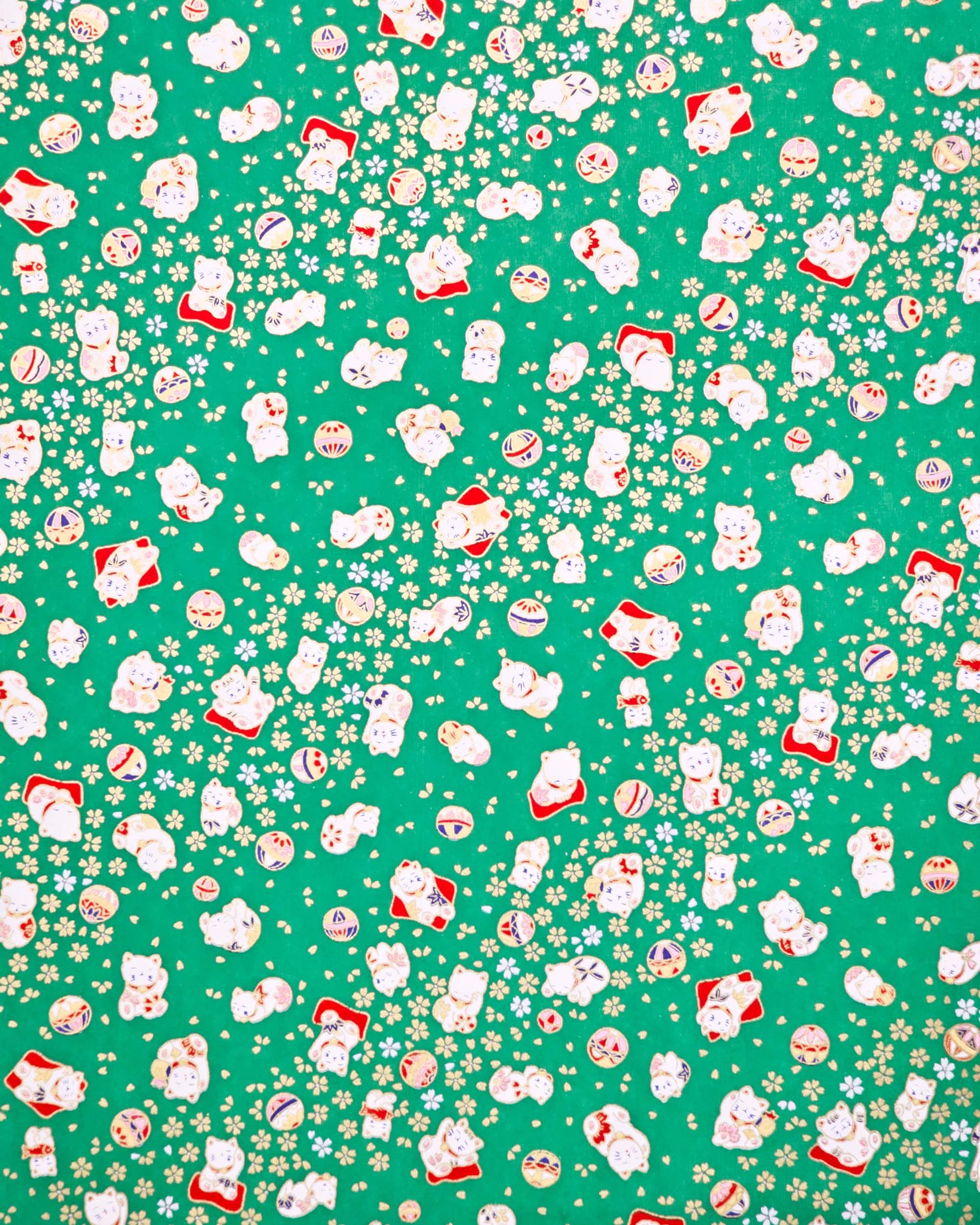 Japanese chiyogami paper featuring assorted white and red Maneki Neko (lucky cats) with small white and gold cherry blossoms and temari balls on a green background with metallic gold details.
