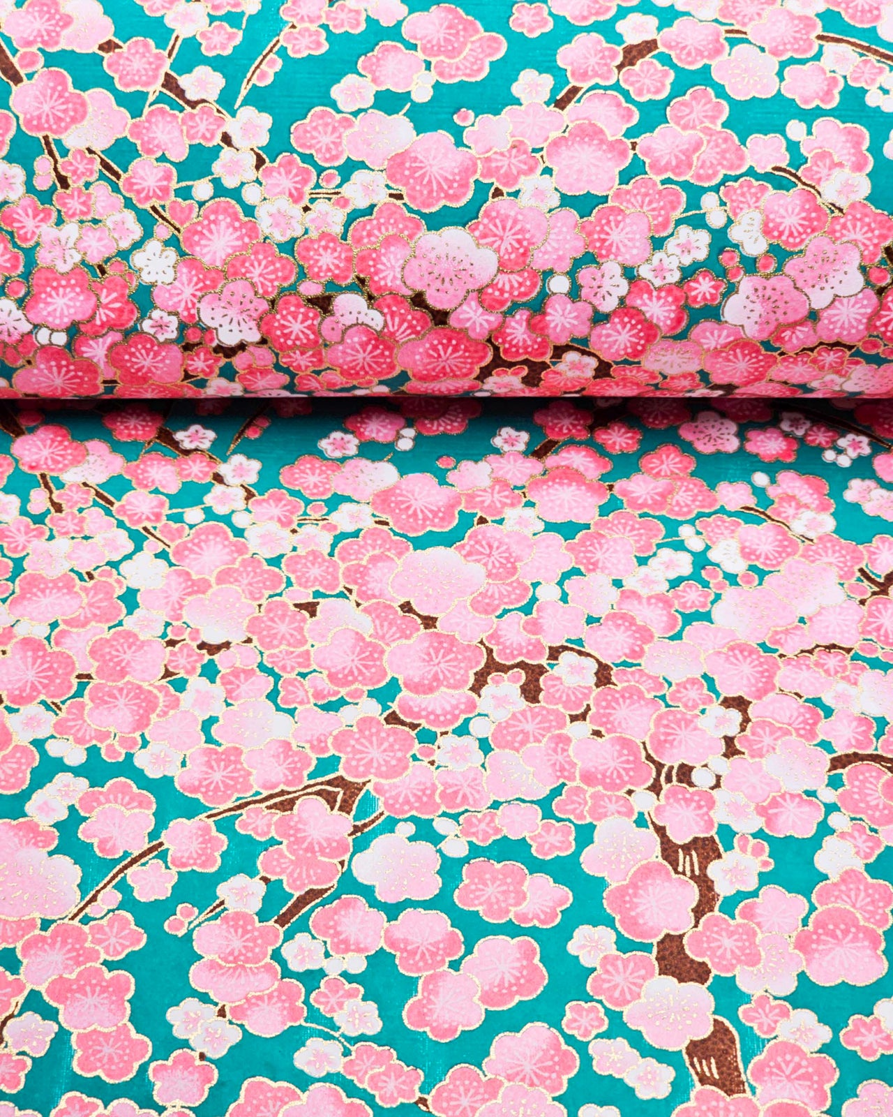 Japanese chiyogami paper featuring pink and white plum blossom trees with brown branches on a teal green background with metallic gold details.