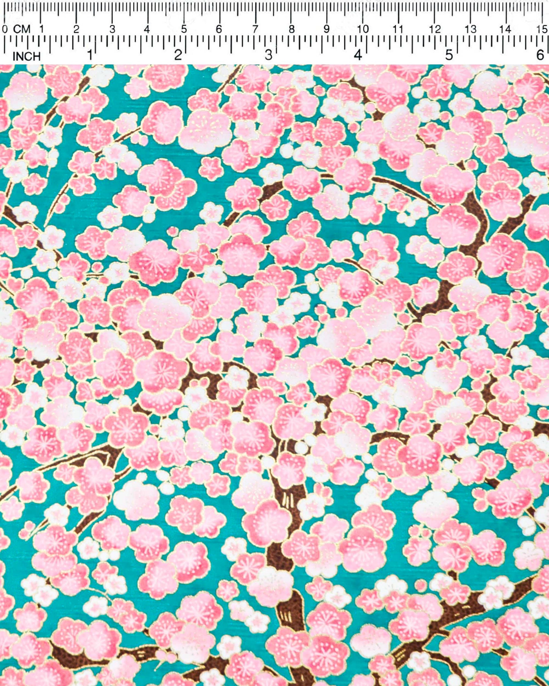 Japanese chiyogami paper featuring pink and white plum blossom trees with brown branches on a teal green background with metallic gold details.