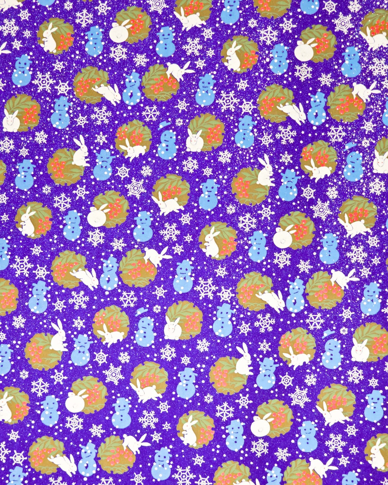 Japanese chiyogami paper featuring light blue snowmen, white rabbits, silver snowflakes, and brown yukiwas with red berries inside on a glitter blue background.