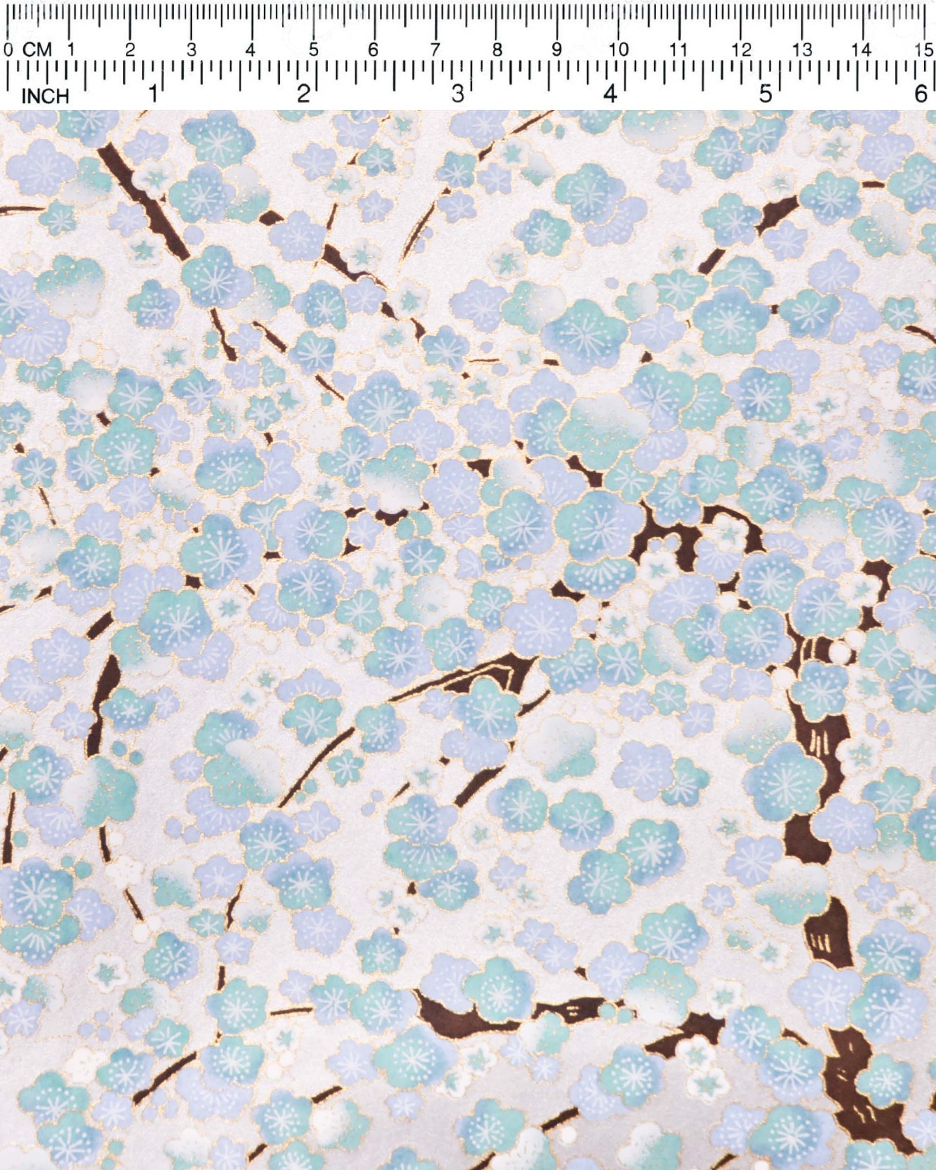 Japanese chiyogami paper featuring light turquoise and white plum blossom trees with brown branches on a silver background with metallic gold details.
