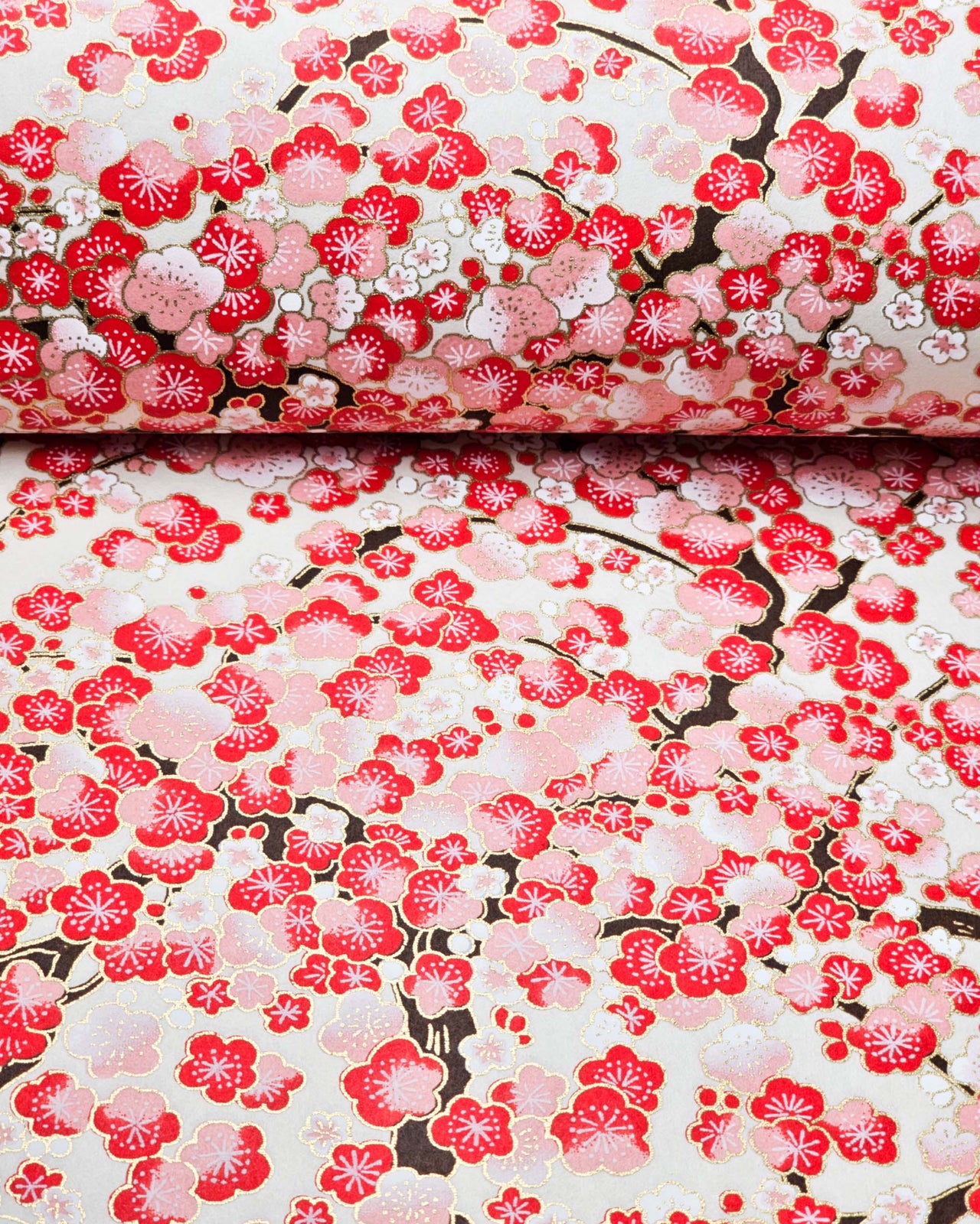 Japanese chiyogami paper featuring red and white plum blossom trees with black branches on a light cream background with metallic gold details.