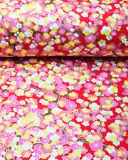 Japanese chiyogami paper featuring pink, yellow, and white plum blossom trees with brown branches on a red background with metallic gold details.
