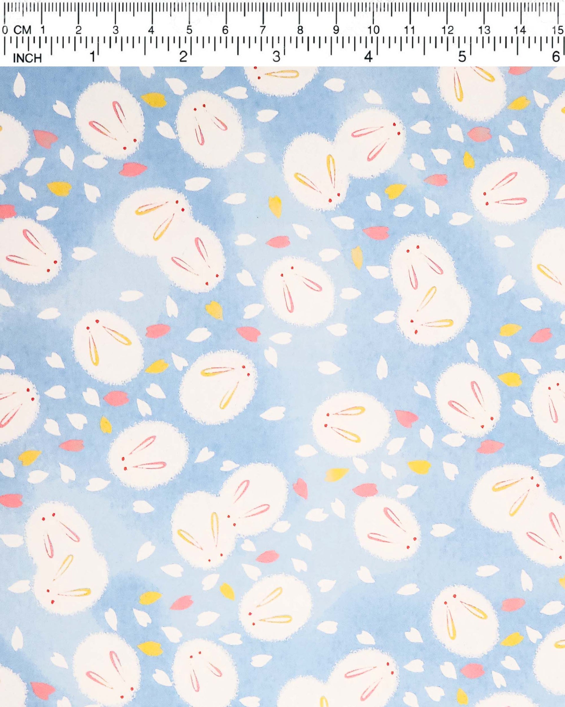 Japanese chiyogami paper featuring round white rabbits with pink and yellow ears surrounded by white, pink, and yellow flower petals on light blue background.