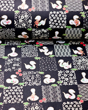 Japanese chiyogami paper featuring white snakes and white assorted traditional Japanese designs in an ichimatsu (checker) design on a black background with metallic gold details. Small red flowers and green leaves accent the design.