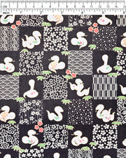 Japanese chiyogami paper featuring white snakes and white assorted traditional Japanese designs in an ichimatsu (checker) design on a black background with metallic gold details. Small red flowers and green leaves accent the design.