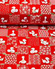 Japanese chiyogami paper featuring white snakes and white assorted traditional Japanese designs in an ichimatsu (checker) design on a red background with metallic gold details. Small pink flowers and green leaves accent the design.