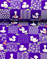 Japanese chiyogami paper featuring white snakes and white assorted traditional Japanese designs in an ichimatsu (checker) design on a blue background with metallic gold details. Small red flowers and green leaves accent the design.