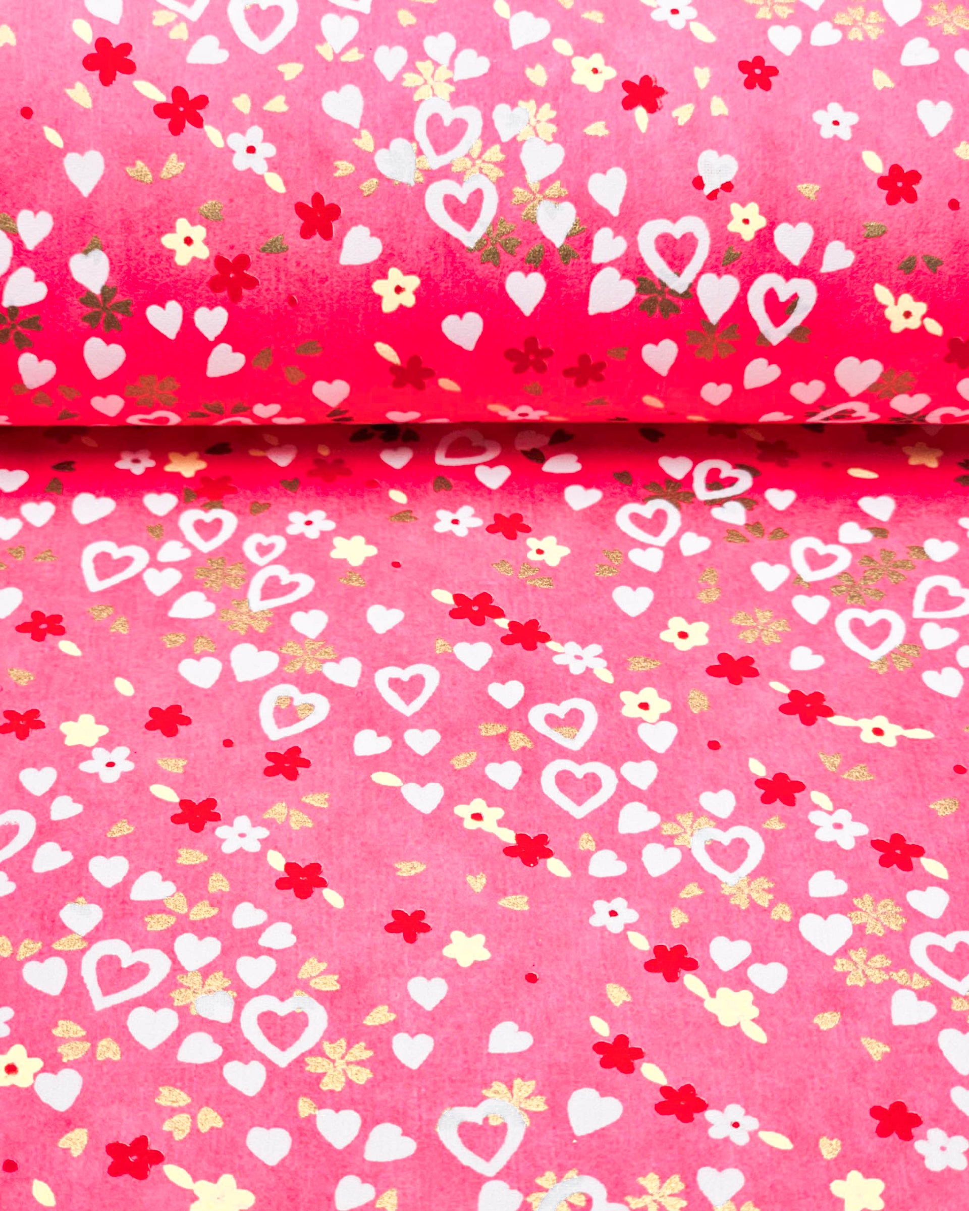 Japanese chiyogami paper featuring white hearts, small white, red, and yellow flowers, and metallic gold cherry blossoms on a pink background.