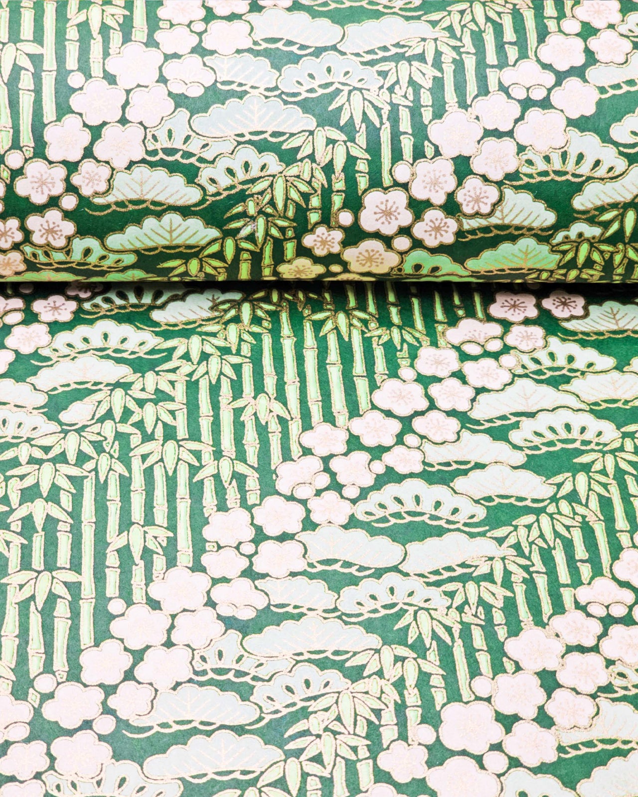 Japanese chiyogami paper featuring cream plum blossoms, light green pine, and green bamboo on green background with metallic gold details.
