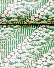 Japanese chiyogami paper featuring cream plum blossoms, light green pine, and green bamboo on green background with metallic gold details.
