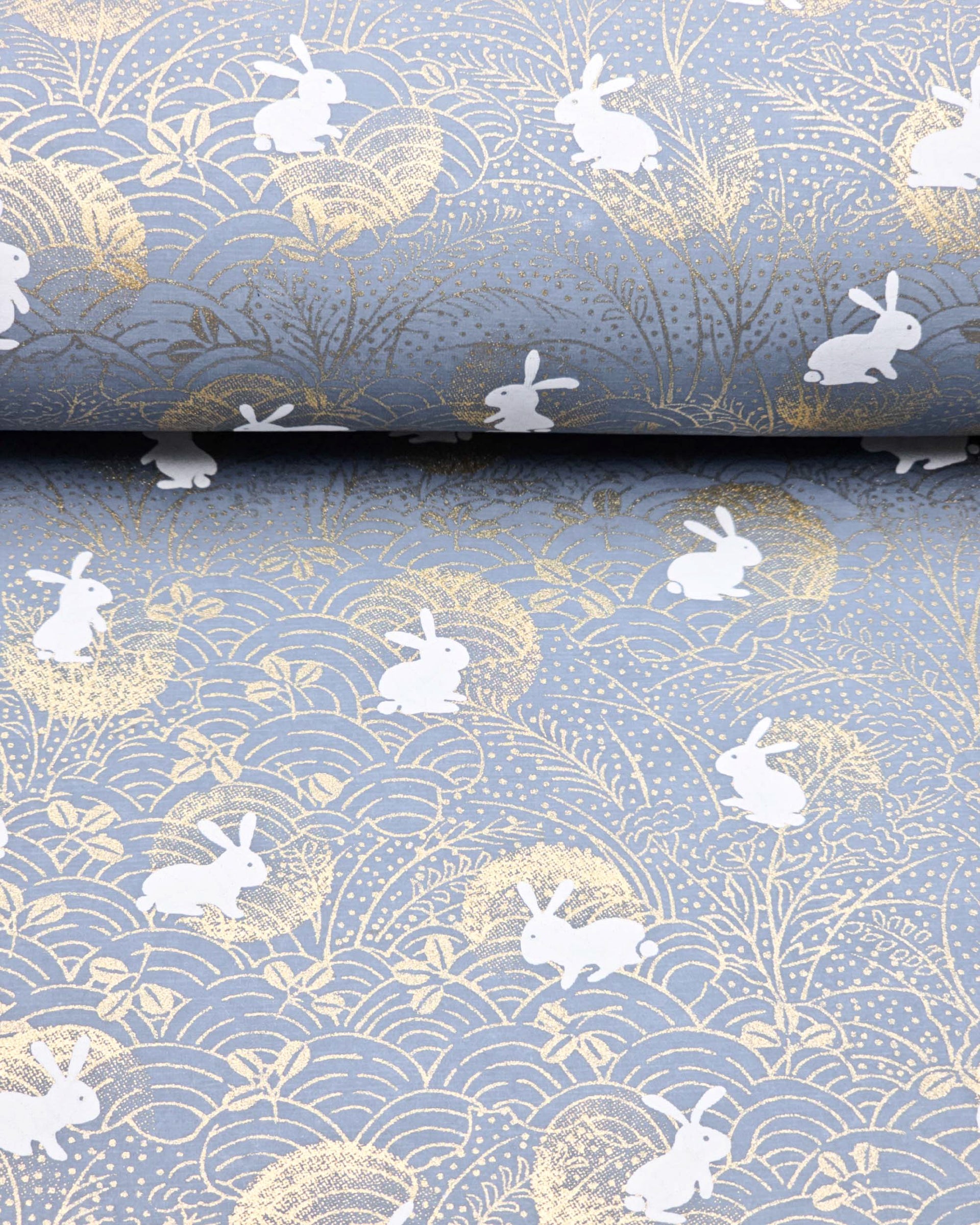 Japanese chiyogami paper featuring white rabbits with gold moons on a blue gray background with metallic gold details.
