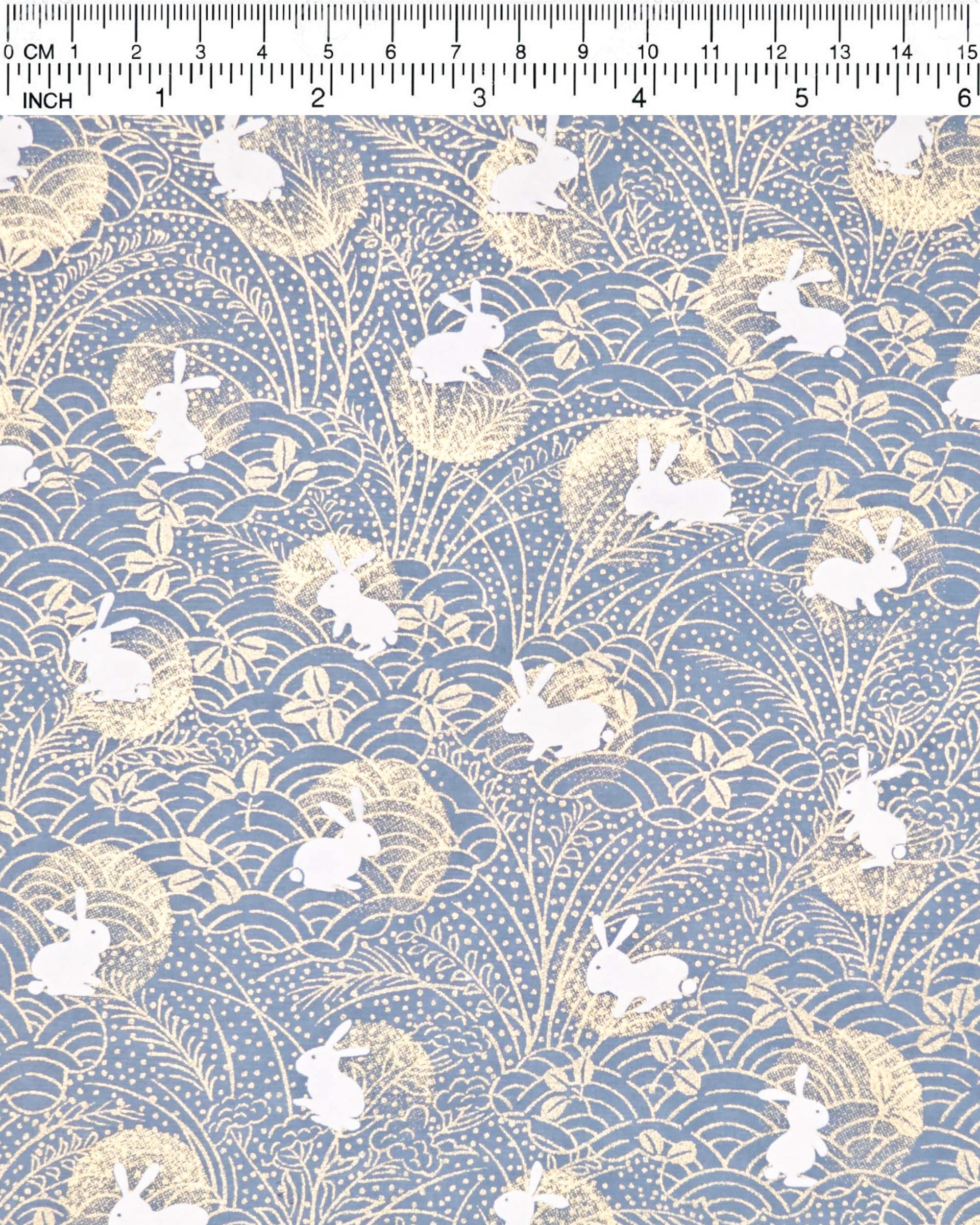 Japanese chiyogami paper featuring white rabbits with gold moons on a blue gray background with metallic gold details.