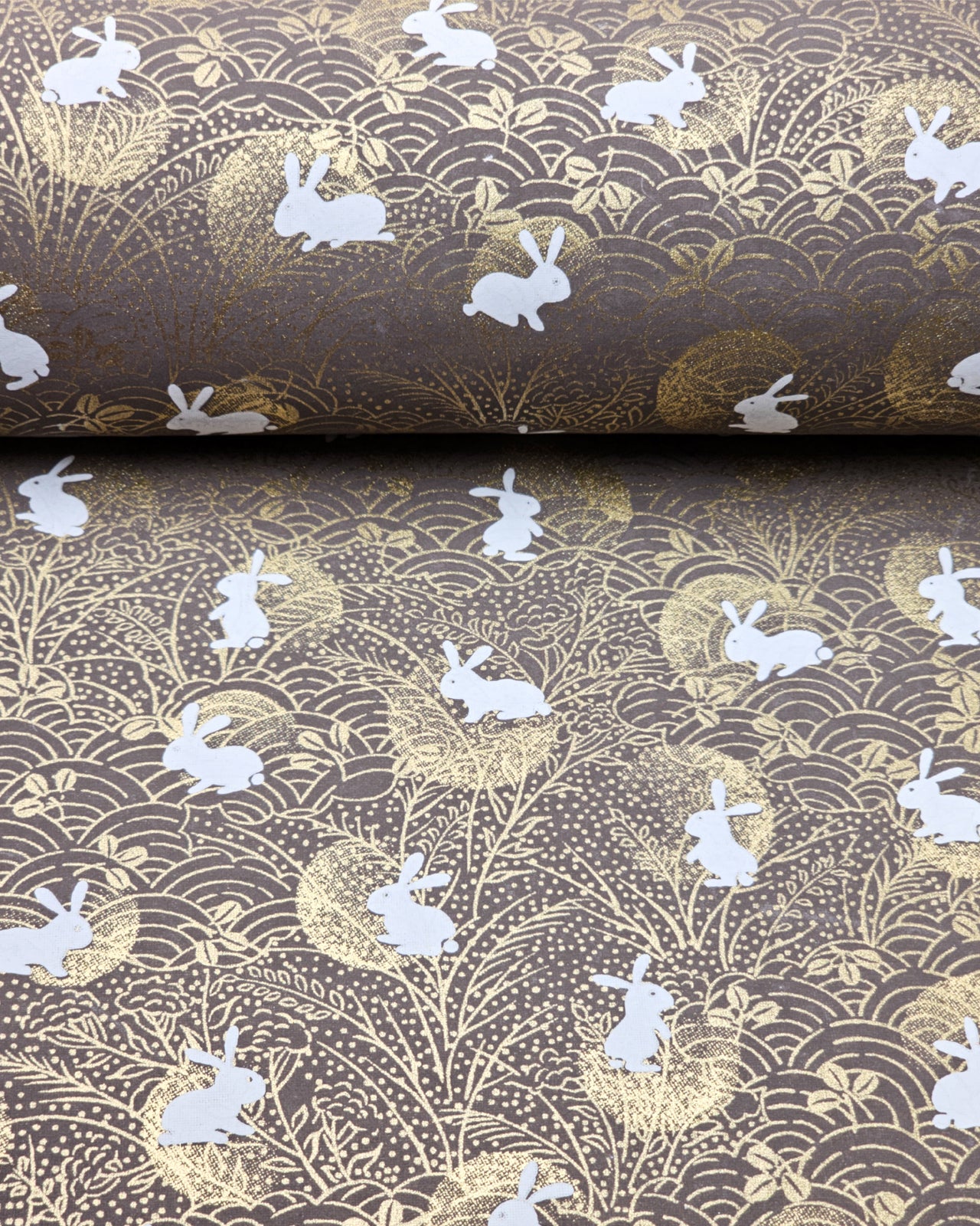 Japanese chiyogami paper featuring white rabbits with gold moons on a brown background with metallic gold details.