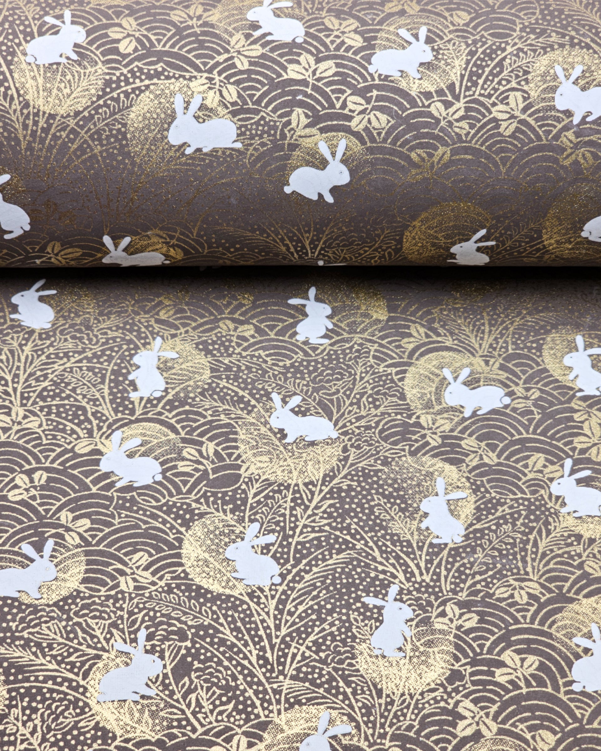 Japanese chiyogami paper featuring white rabbits with gold moons on a brown background with metallic gold details.