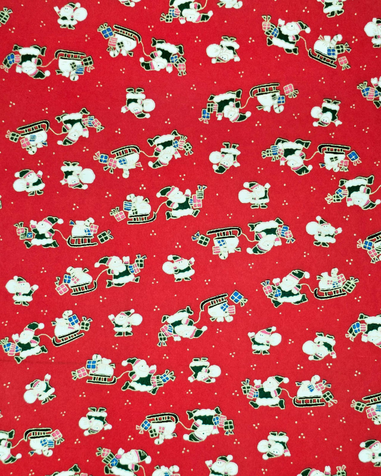 Japanese chiyogami paper featuring cartoon Santas in green outfits pulling sleds with presents and carrying sacks of presents on a red background with metallic gold details. 