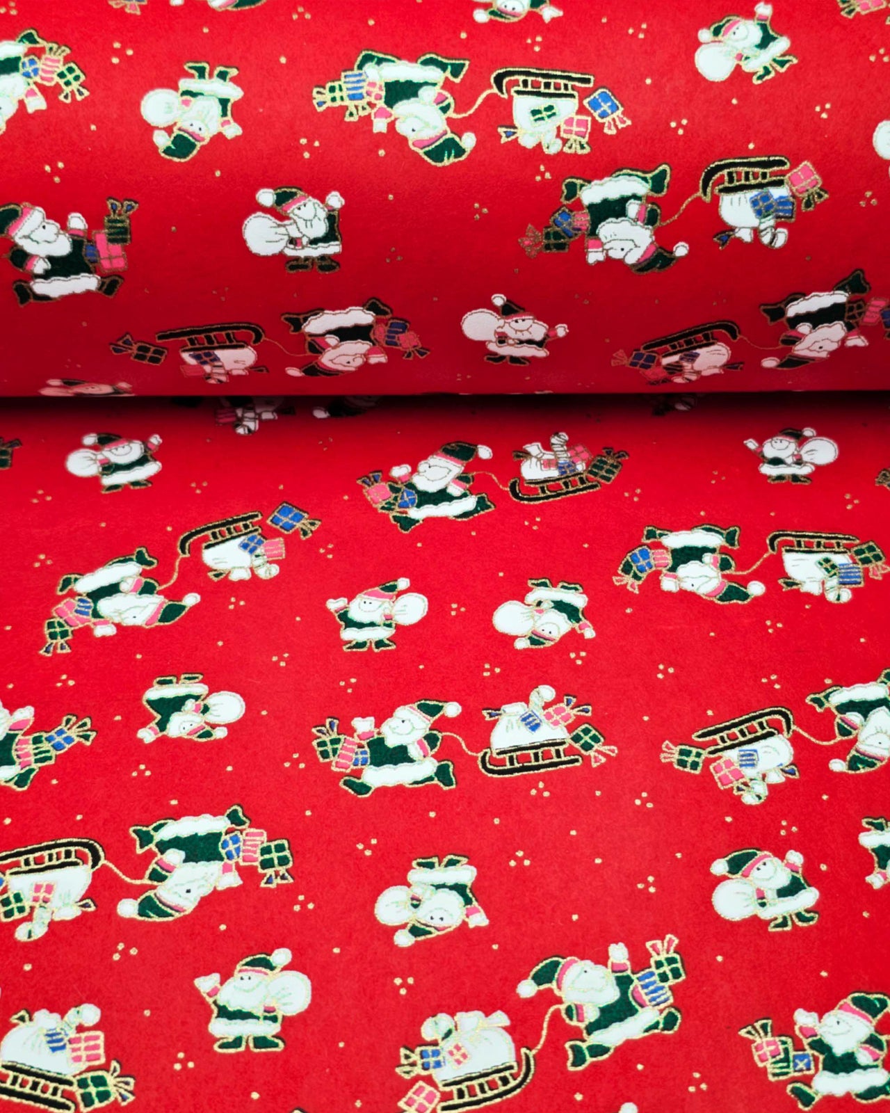 Japanese chiyogami paper featuring cartoon Santas in green outfits pulling sleds with presents and carrying sacks of presents on a red background with metallic gold details. 