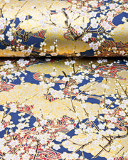 Japanese chiyogami paper featuring small white plum blossom branches with red and gold swirls on a dark blue and gold background with metallic gold details.