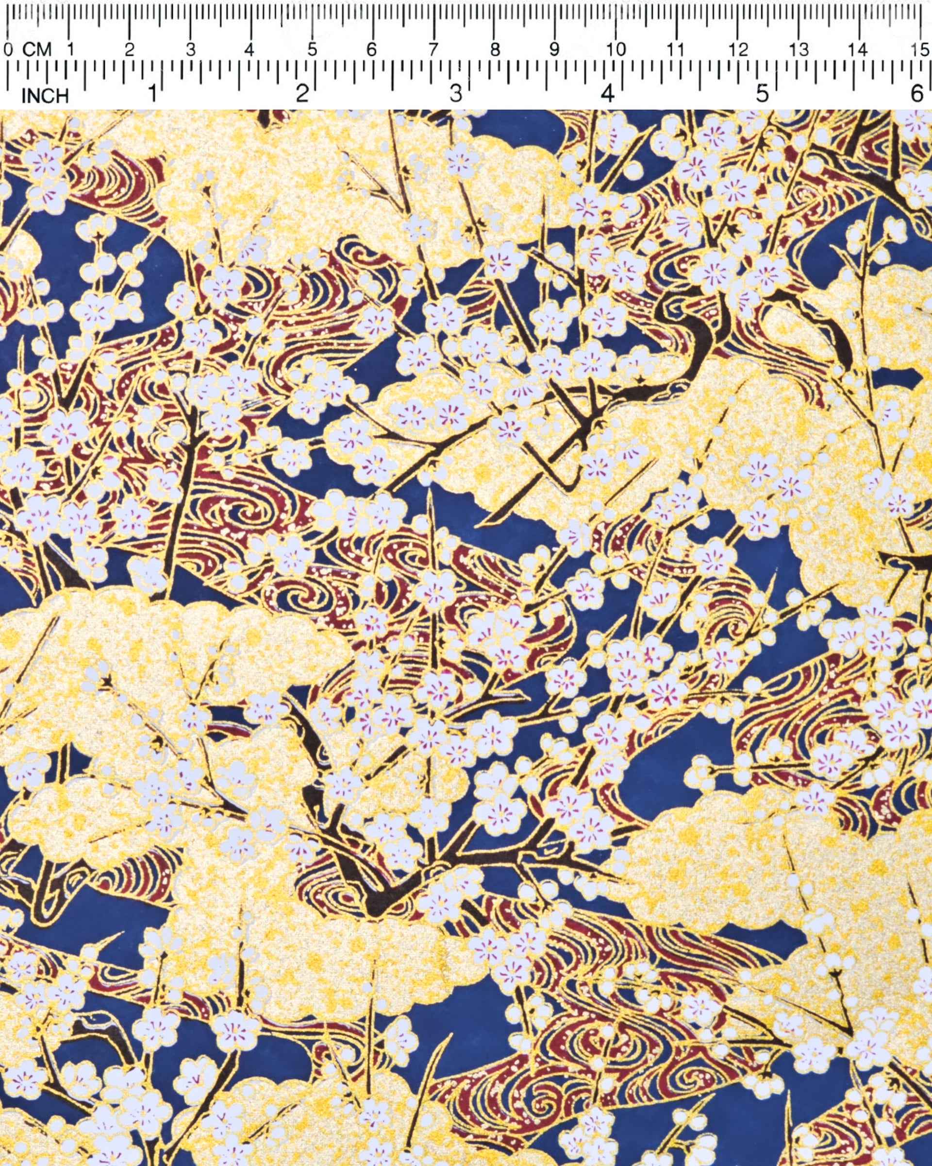Japanese chiyogami paper featuring small white plum blossom branches with red and gold swirls on a dark blue and gold background with metallic gold details.