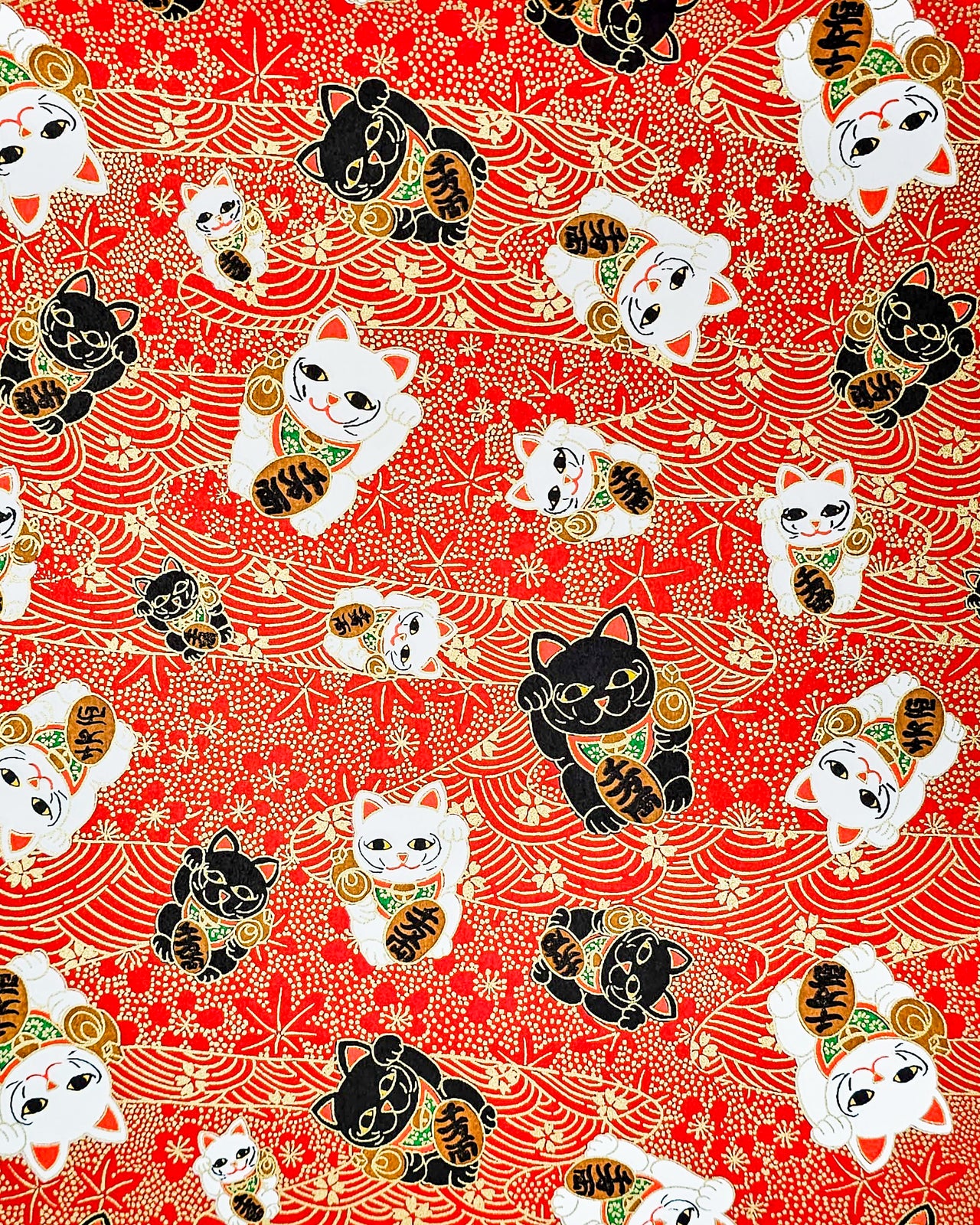 Japanese chiyogami paper featuring large black and white maneki neko (lucky cats) on a red background with metallic gold details. The red background has metallic gold cherry blossoms, plum blossoms, maples leaves, and wave crests.