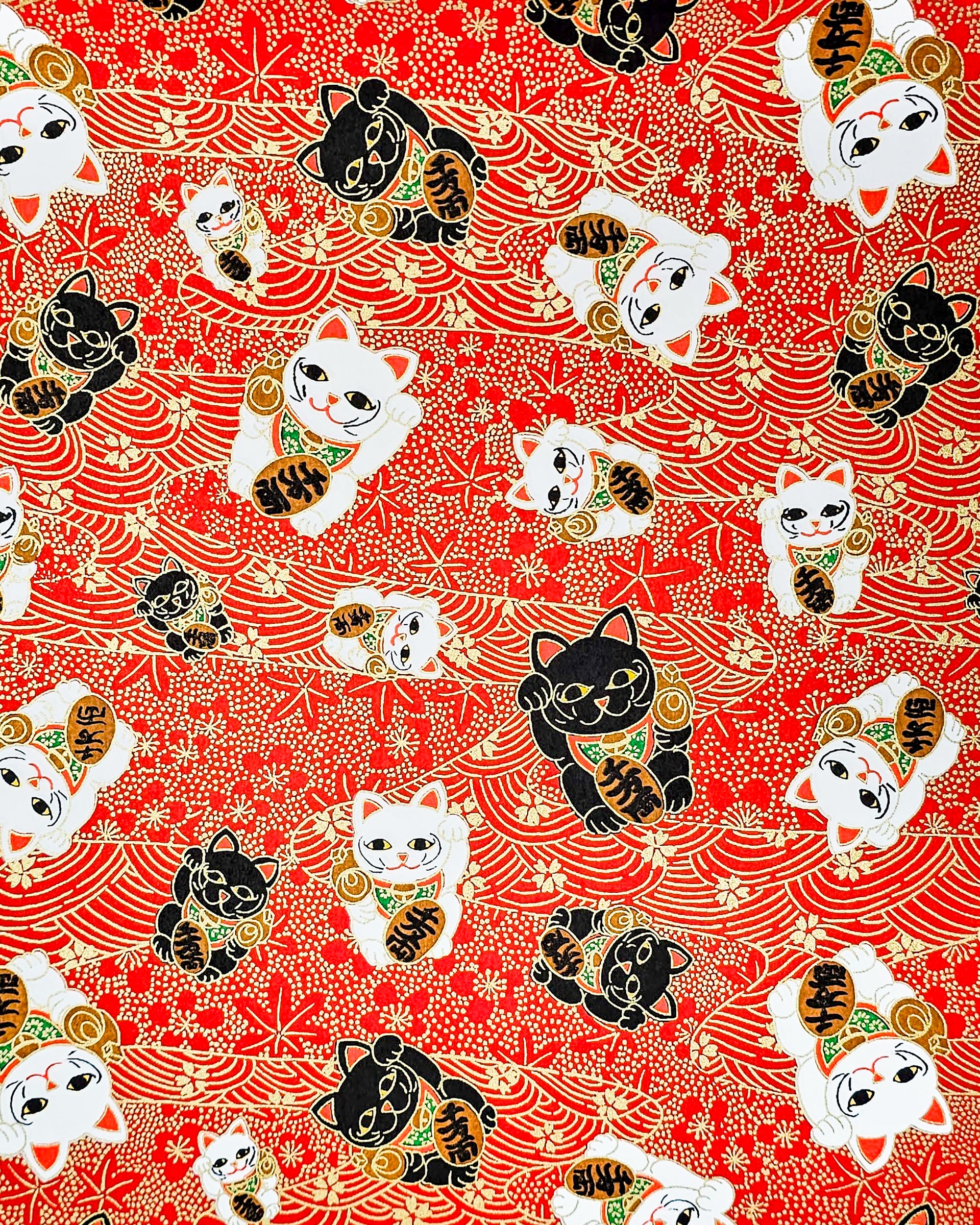 Japanese chiyogami paper featuring large black and white maneki neko (lucky cats) on a red background with metallic gold details. The red background has metallic gold cherry blossoms, plum blossoms, maples leaves, and wave crests.