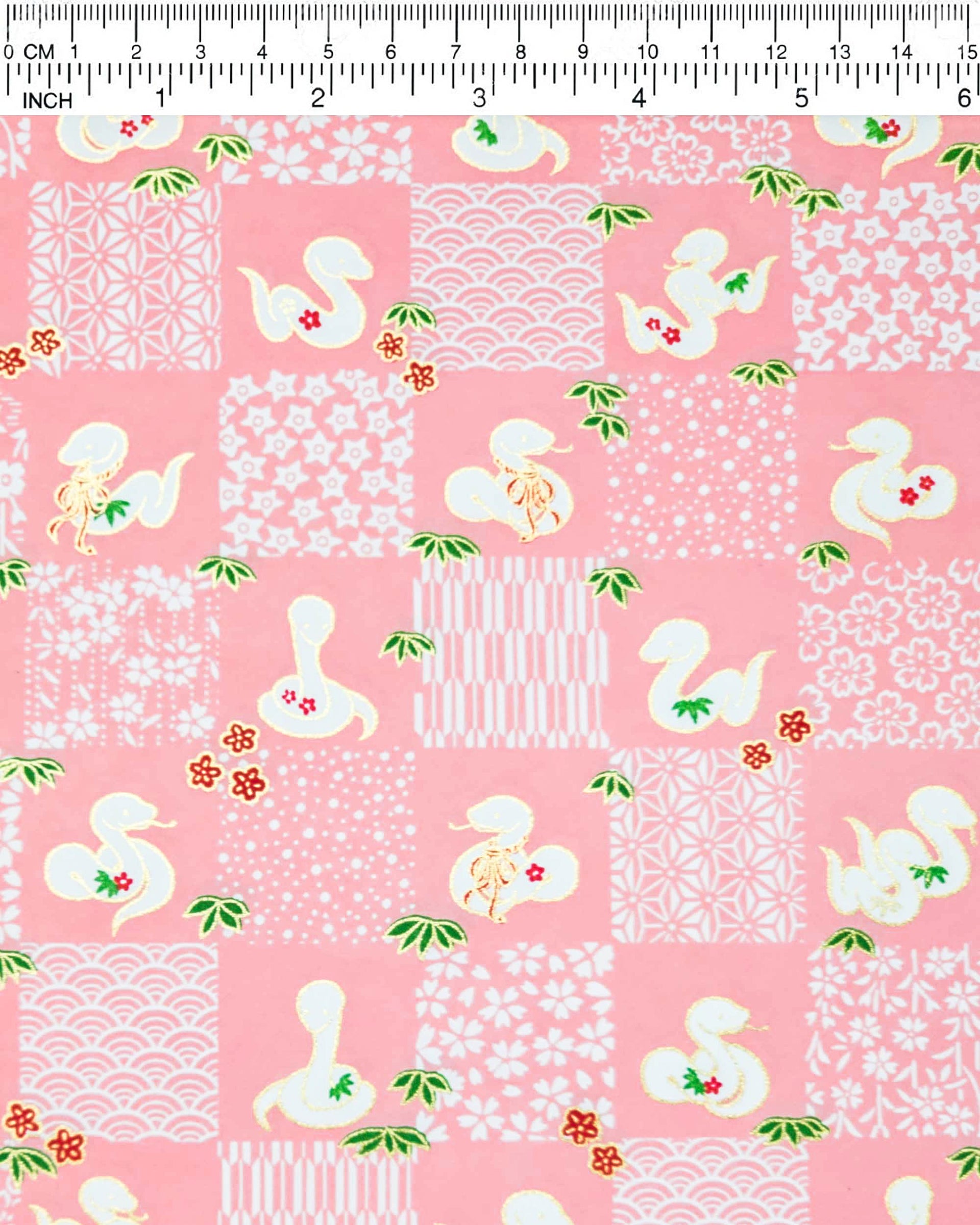Japanese chiyogami paper featuring white snakes and white assorted traditional Japanese designs in an ichimatsu (checker) design on a pink background with metallic gold details.