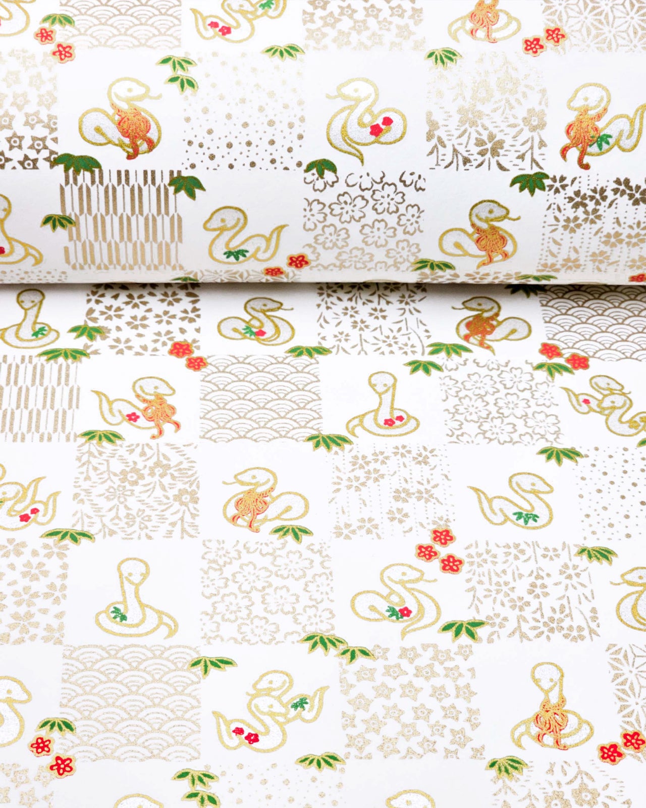 Japanese chiyogami paper featuring silver snakes and gold assorted traditional Japanese designs in an ichimatsu (checker) design on a white background with metallic gold details. Small red plum blossoms and green bamboo leaves are scattered throughout the design.