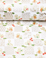 Japanese chiyogami paper featuring silver snakes and gold assorted traditional Japanese designs in an ichimatsu (checker) design on a white background with metallic gold details. Small red plum blossoms and green bamboo leaves are scattered throughout the design.
