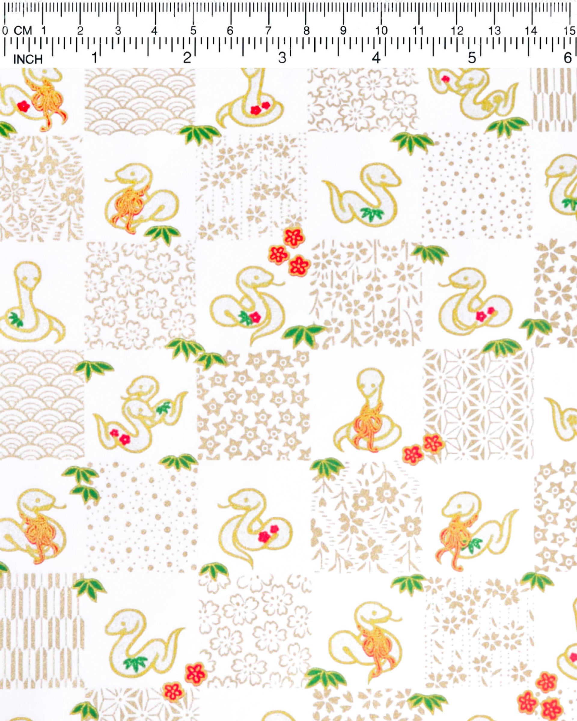 Japanese chiyogami paper featuring silver snakes and gold assorted traditional Japanese designs in an ichimatsu (checker) design on a white background with metallic gold details. Small red plum blossoms and green bamboo leaves are scattered throughout the design.