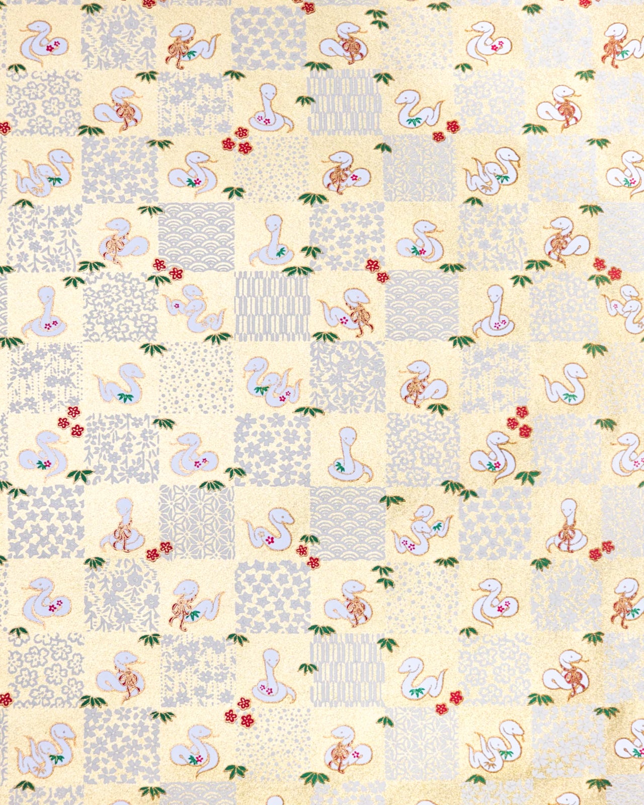 Japanese chiyogami paper featuring white snakes and white assorted traditional Japanese designs in an ichimatsu (checker) design on a gold background with metallic gold details. Small red plum blossoms and green bamboo leaves are scattered throughout the design.