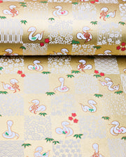 Japanese chiyogami paper featuring white snakes and white assorted traditional Japanese designs in an ichimatsu (checker) design on a gold background with metallic gold details. Small red plum blossoms and green bamboo leaves are scattered throughout the design.