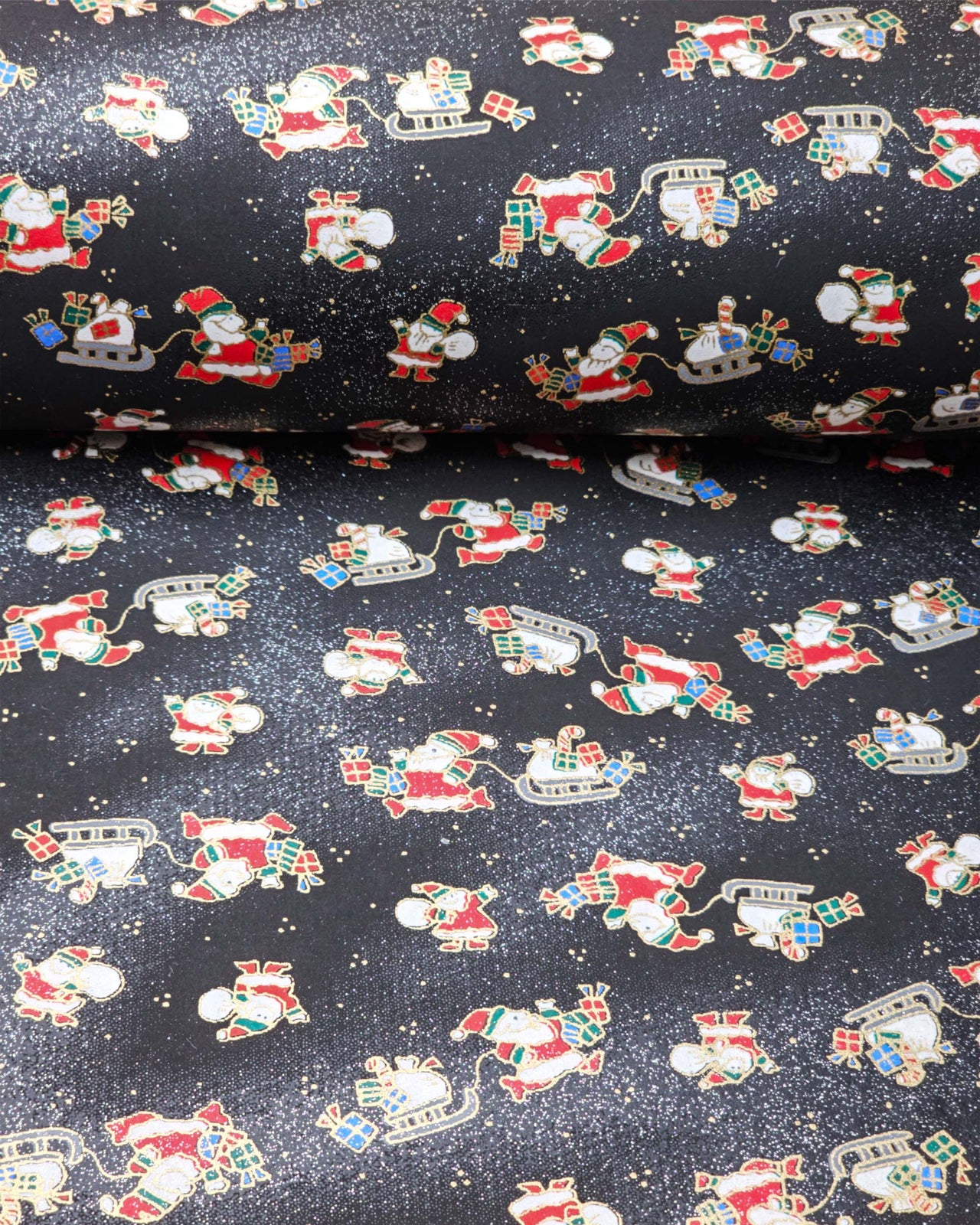 Japanese chiyogami paper featuring Santa and his sleigh on a black and background with metallic gold accents and metallic silver glitter.