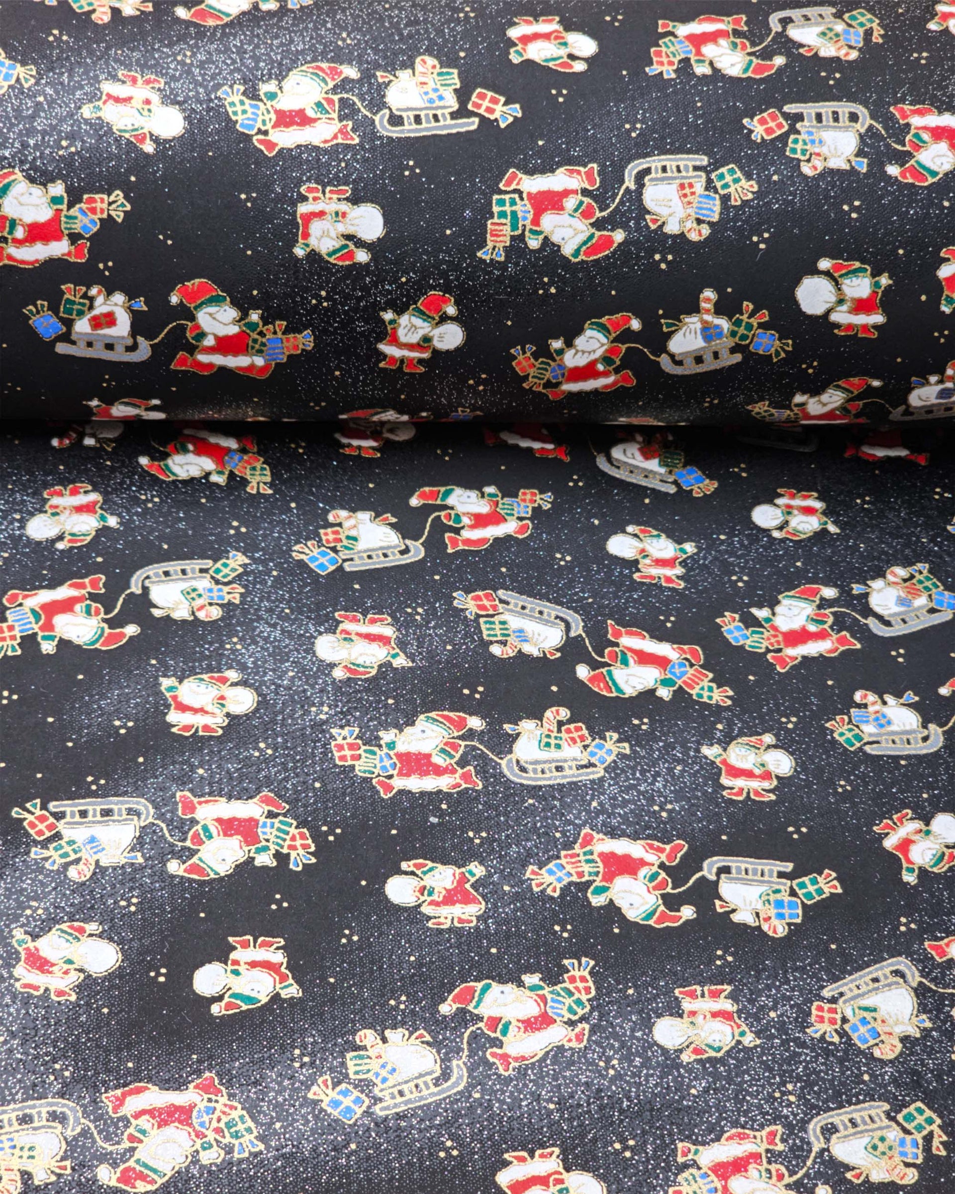 Japanese chiyogami paper featuring Santa and his sleigh on a black and background with metallic gold accents and metallic silver glitter.
