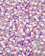 Japanese chiyogami paper featuring purple, red, white, and yellow plum blossoms with beige branches and light green leaves on a dark purple background with metallic gold details.