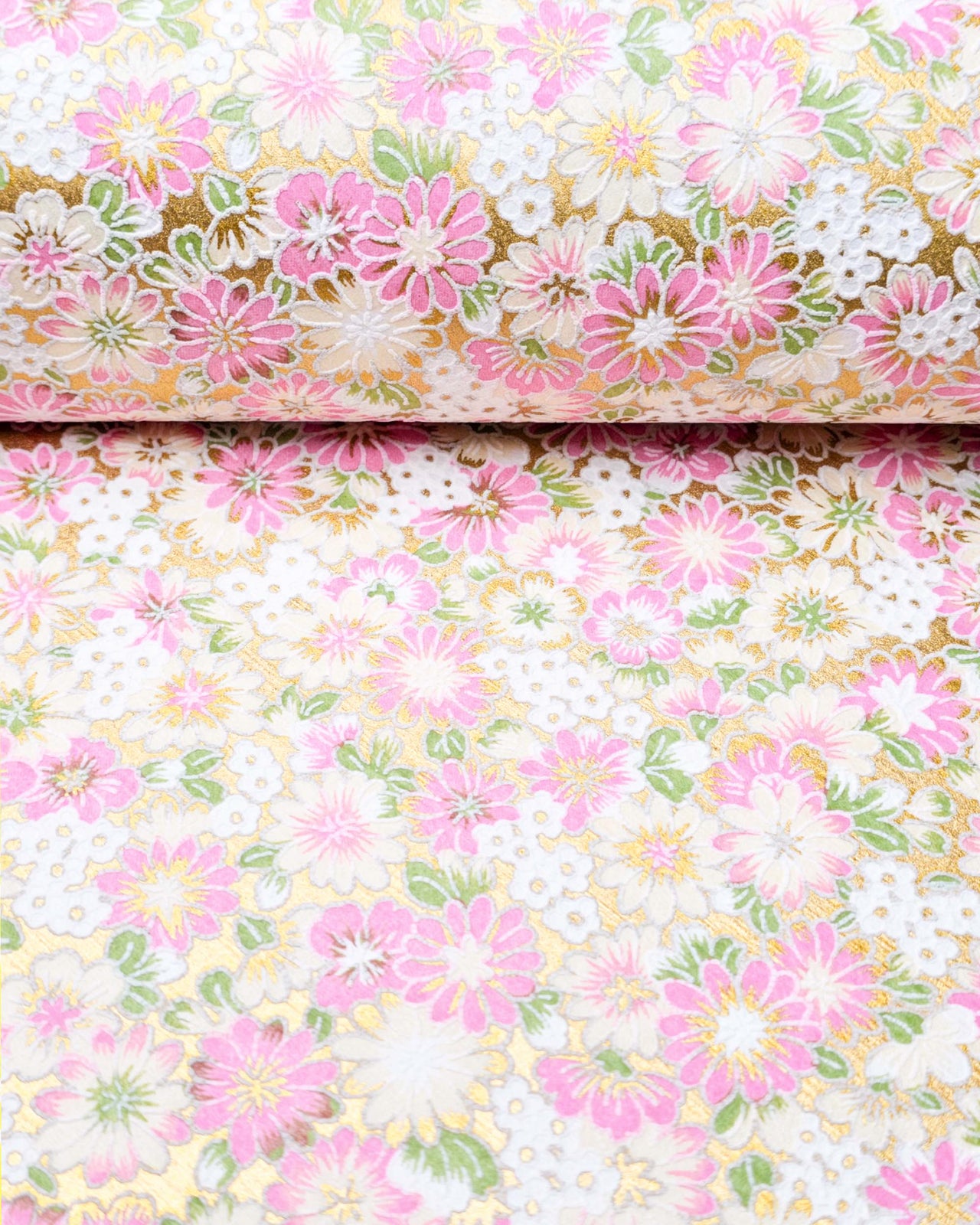 Japanese chiyogami paper featuring textured white and pink mum flowers on a metallic gold background. The lines on the flowers are raised.