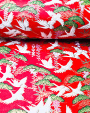 Japanese chiyogami paper featuring white flying cranes, purple and white wisteria, and green pine on a pearlescent red background with metallic gold details.