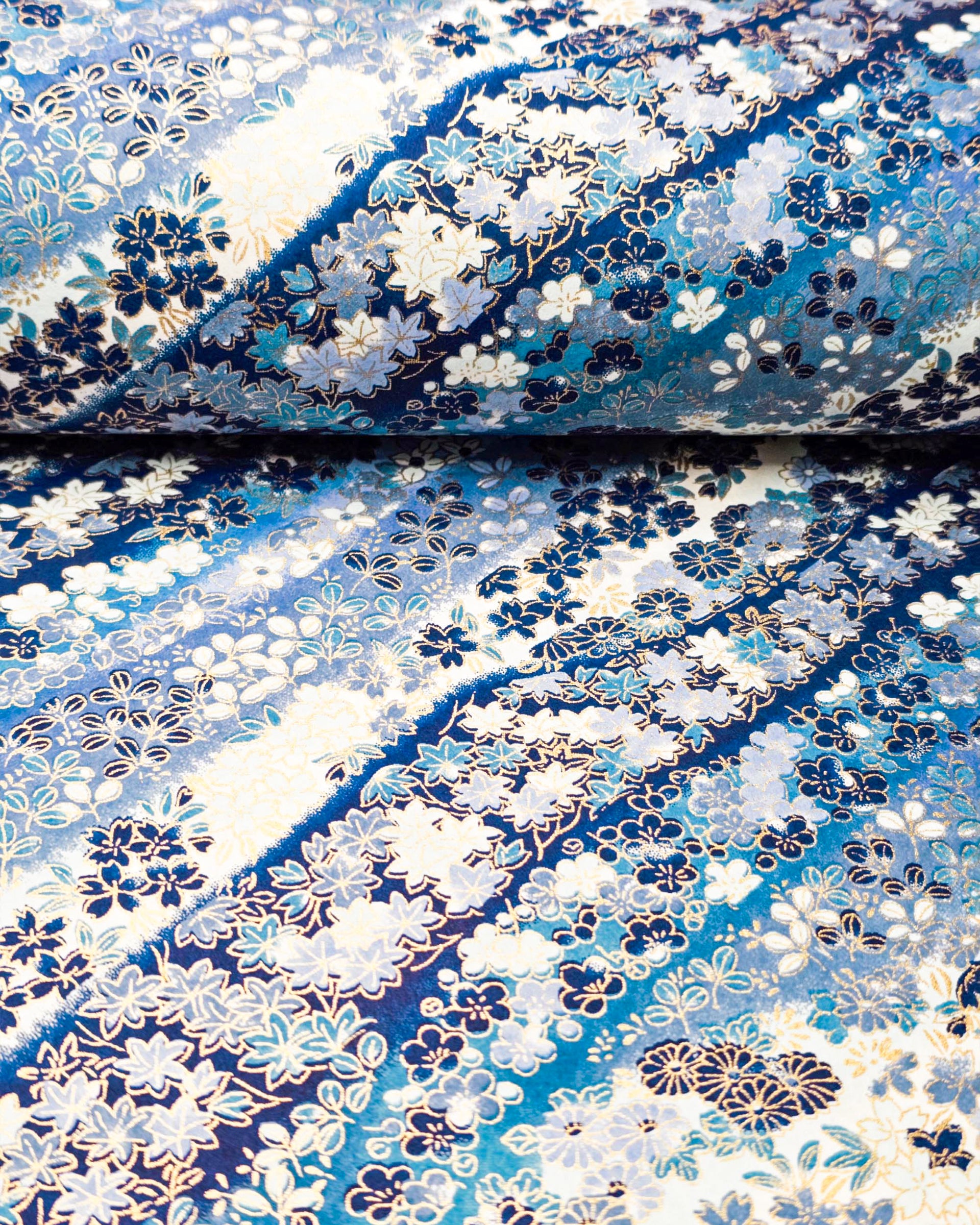 Japanese chiyogami paper featuring assorted blue and white flowers on a blue background with metallic gold accents.