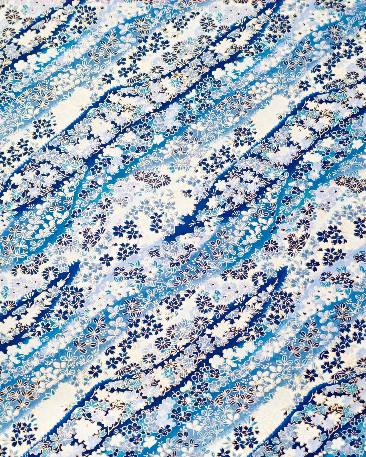 Japanese chiyogami paper featuring an assortment of blue and white traditional Japanese flowers and leaves on a blue and white gradient background with metallic gold details.