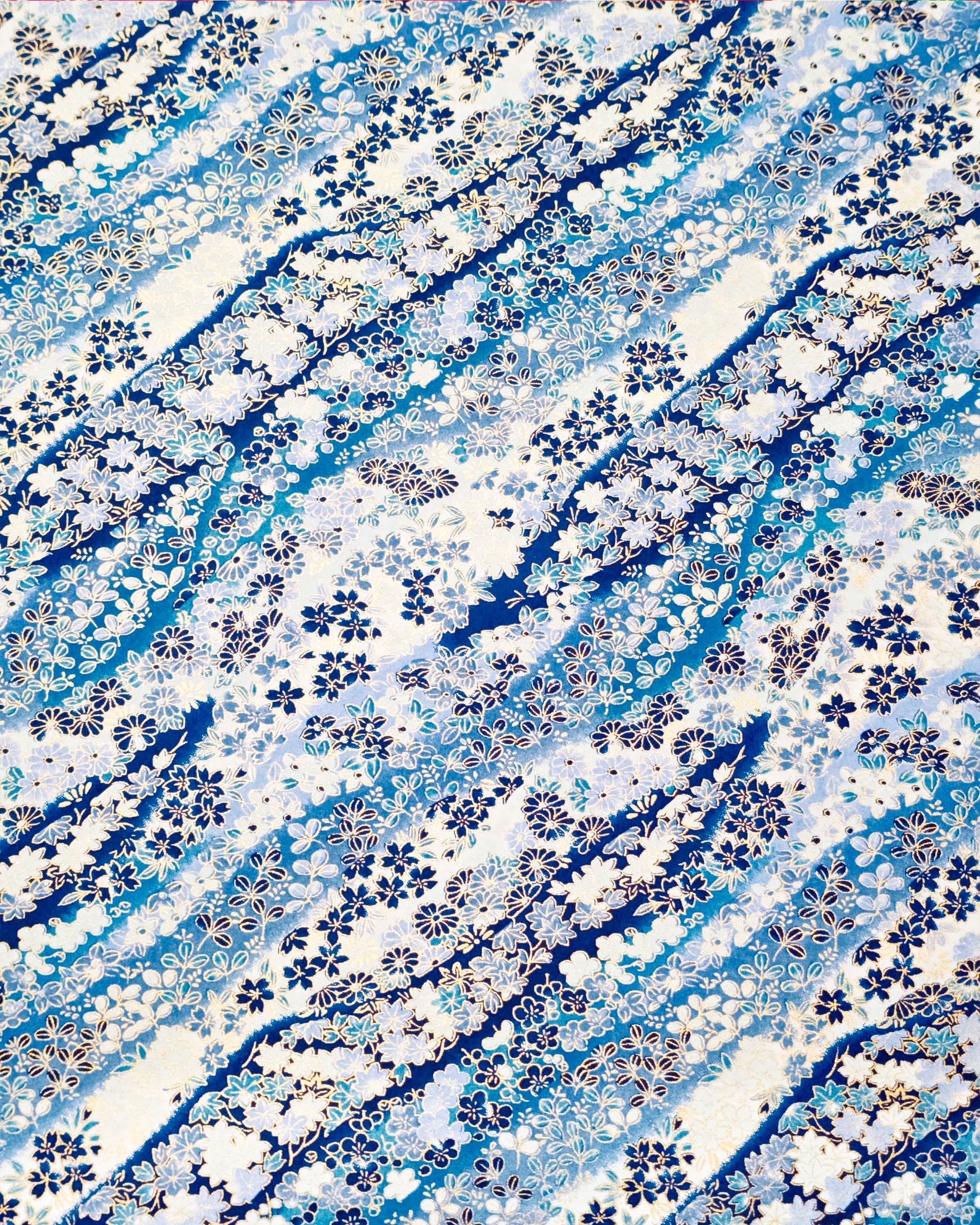Japanese chiyogami paper featuring an assortment of blue and white traditional Japanese flowers and leaves on a blue and white gradient background with metallic gold details.