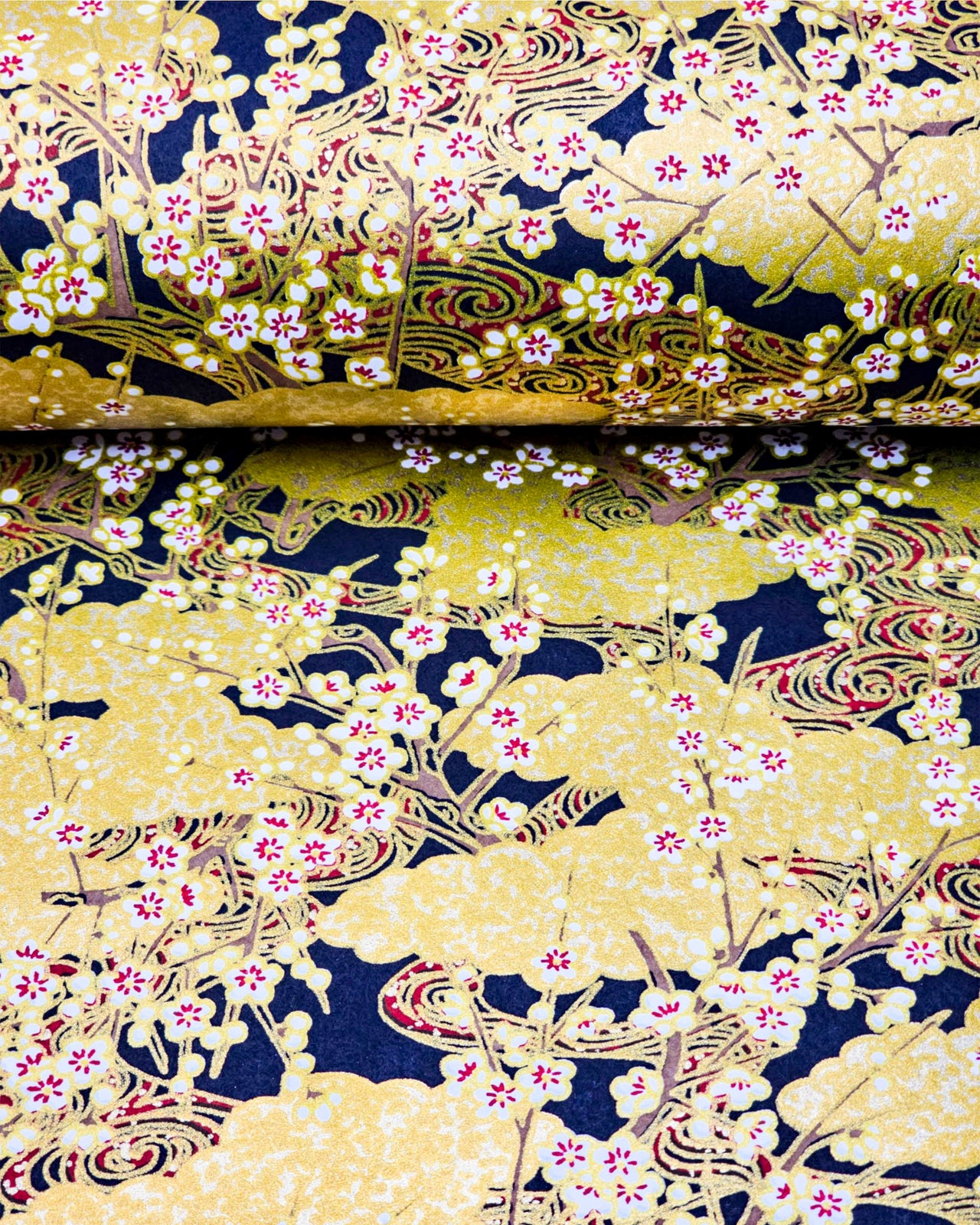 Japanese chiyogami paper featuring white plum blossom branches on a black and gold background with metallic gold accents.