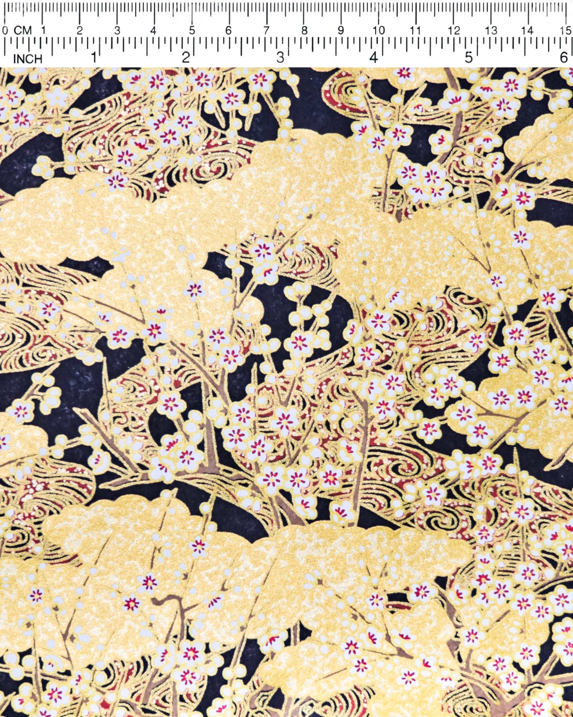 Japanese chiyogami paper featuring white plum blossom branches on a black and gold background with metallic gold accents.