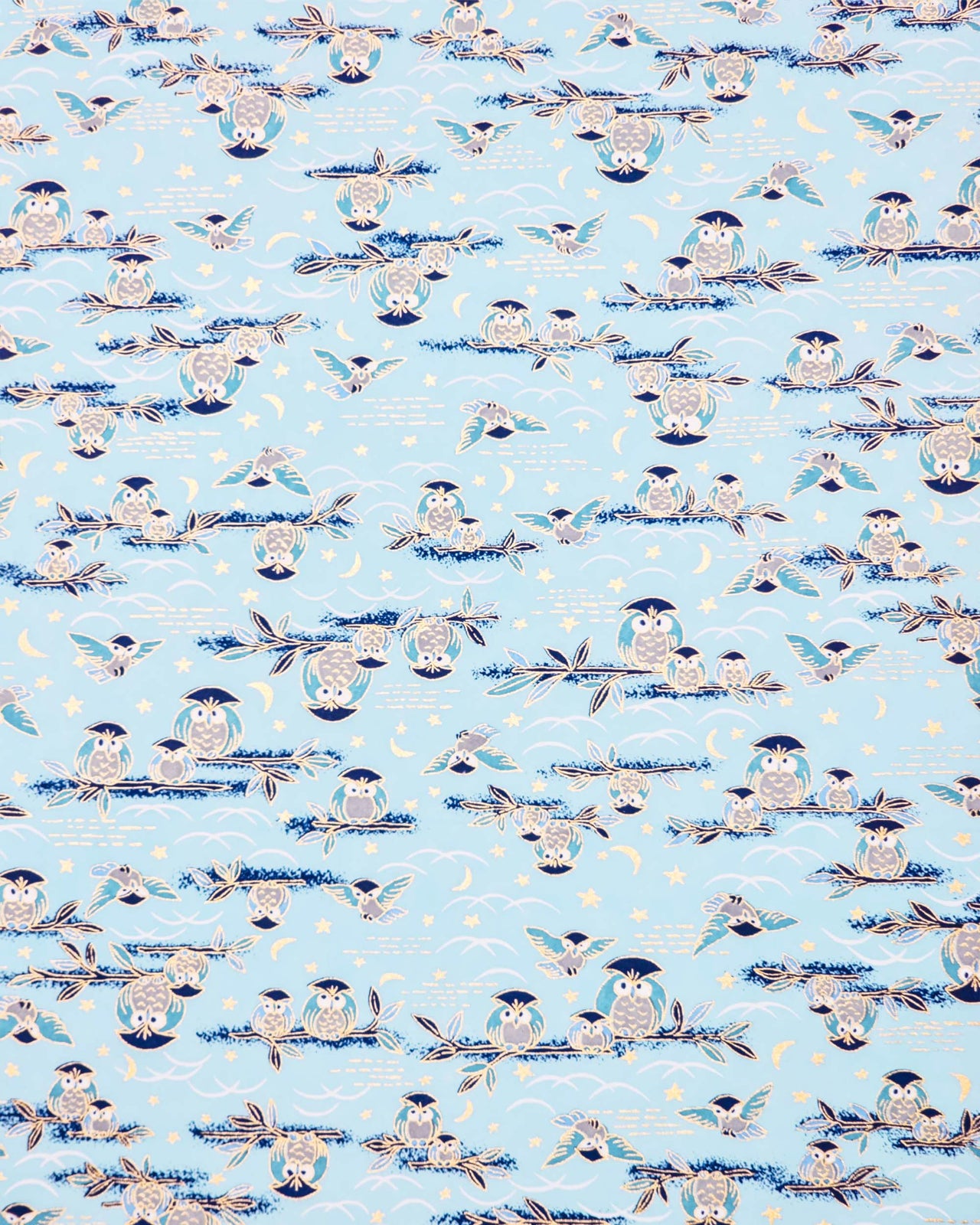 Japanese chiyogami paper featuring blue and gray owls perched on branches and flying around with a light blue night sky background adorned with small metallic gold stars and crescent moons.