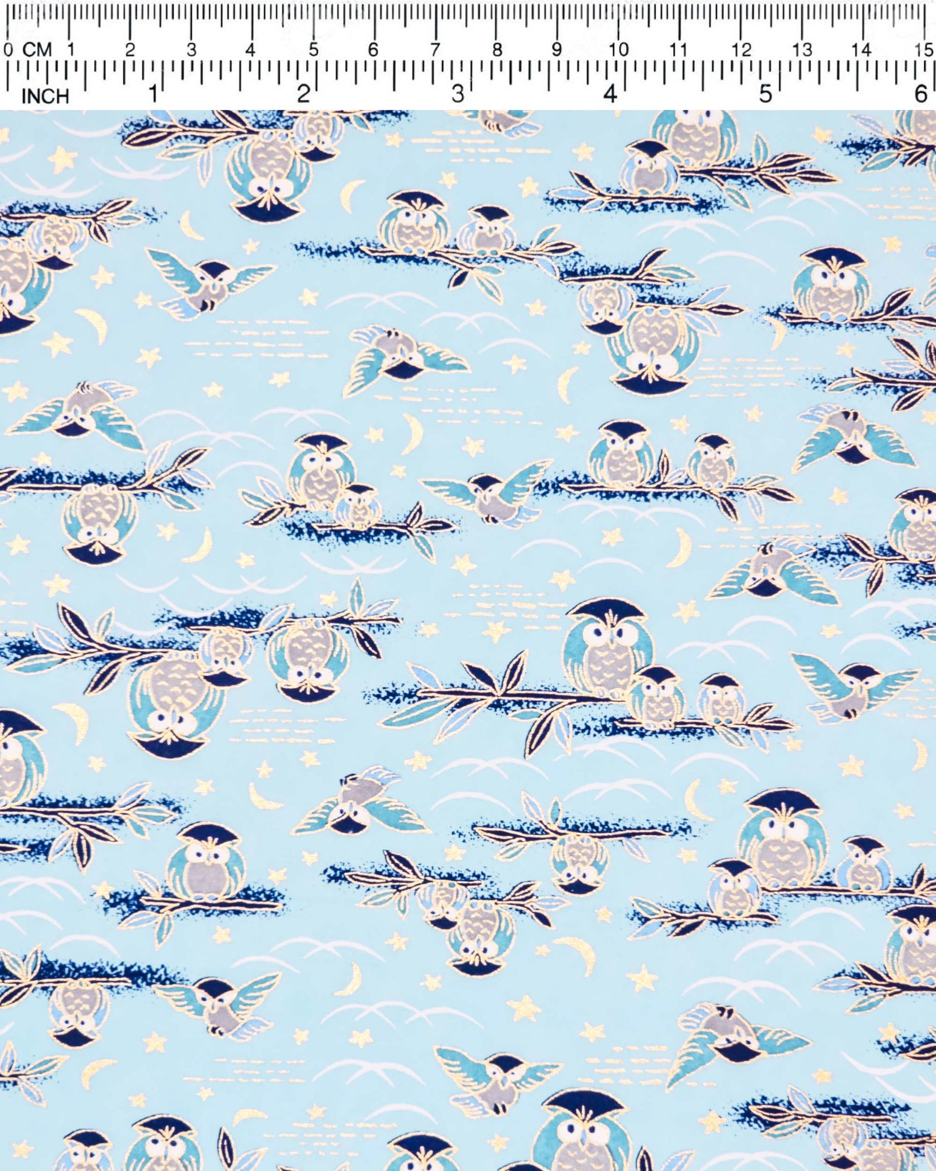 Japanese chiyogami paper featuring blue and gray owls perched on branches and flying around with a light blue night sky background adorned with small metallic gold stars and crescent moons.