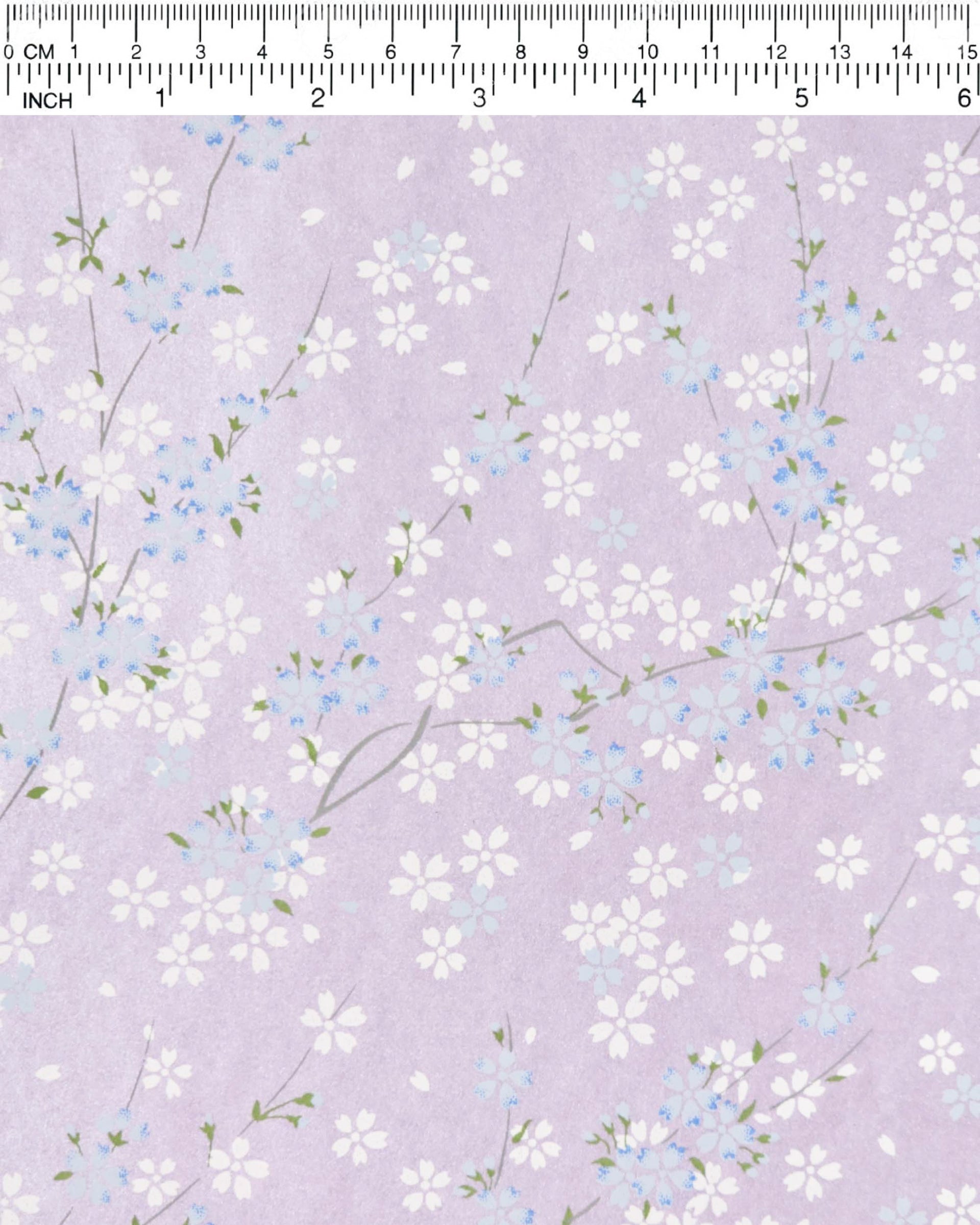 Japanese chiyogami paper featuring light blue and white cherry blossoms with green leaves and branches on a pearlescent light purple background.