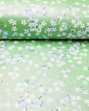 Japanese chiyogami paper featuring light blue and white cherry blossoms with green leaves and branches on a pearlescent green background.